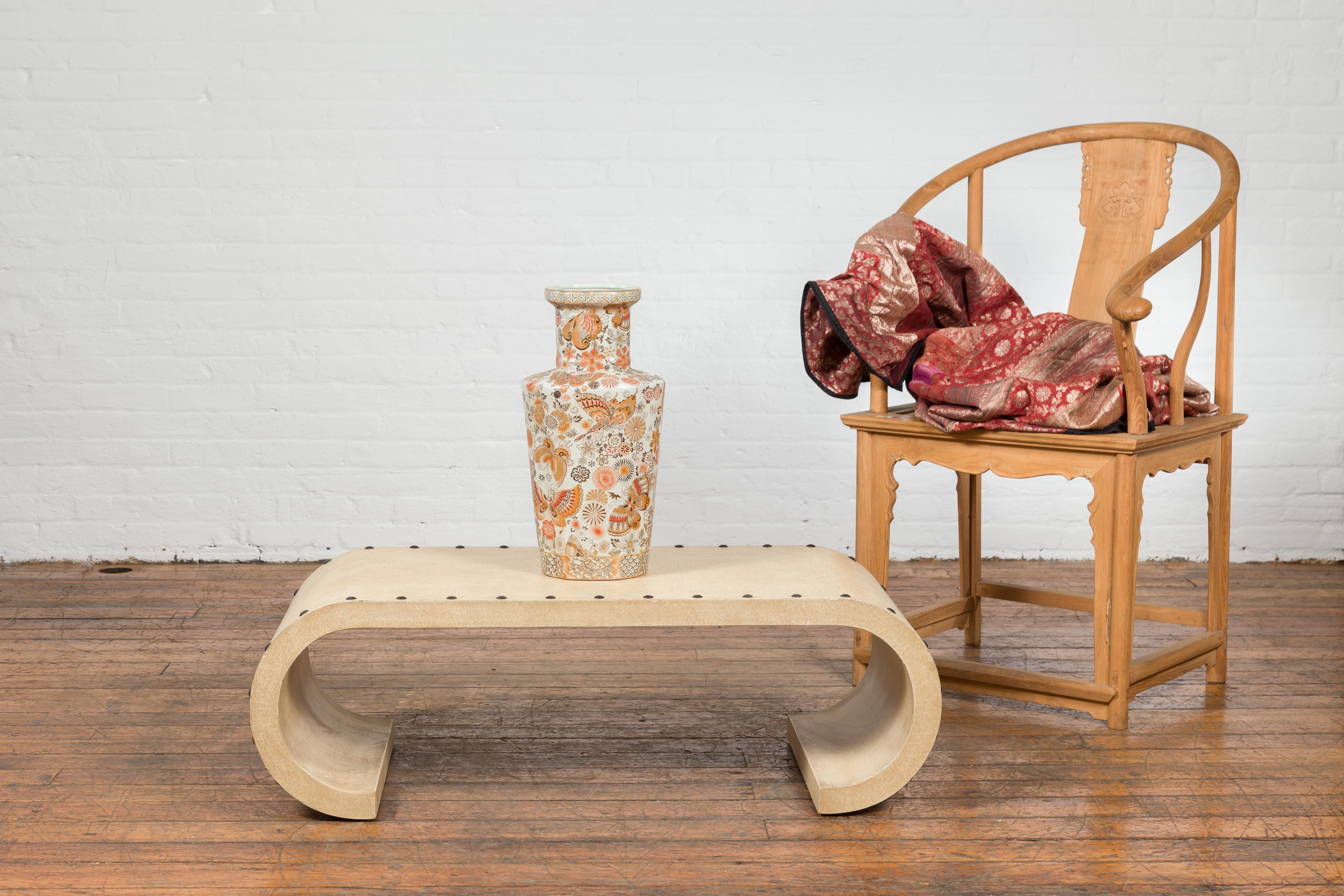 A contemporary Burmese scroll coffee table from the 21st century, with underglaze beige snakeskin patina and round nailheads. Created in Burma, this contemporary coffee table charms us with its scrolling design and beige snakeskin appearance.