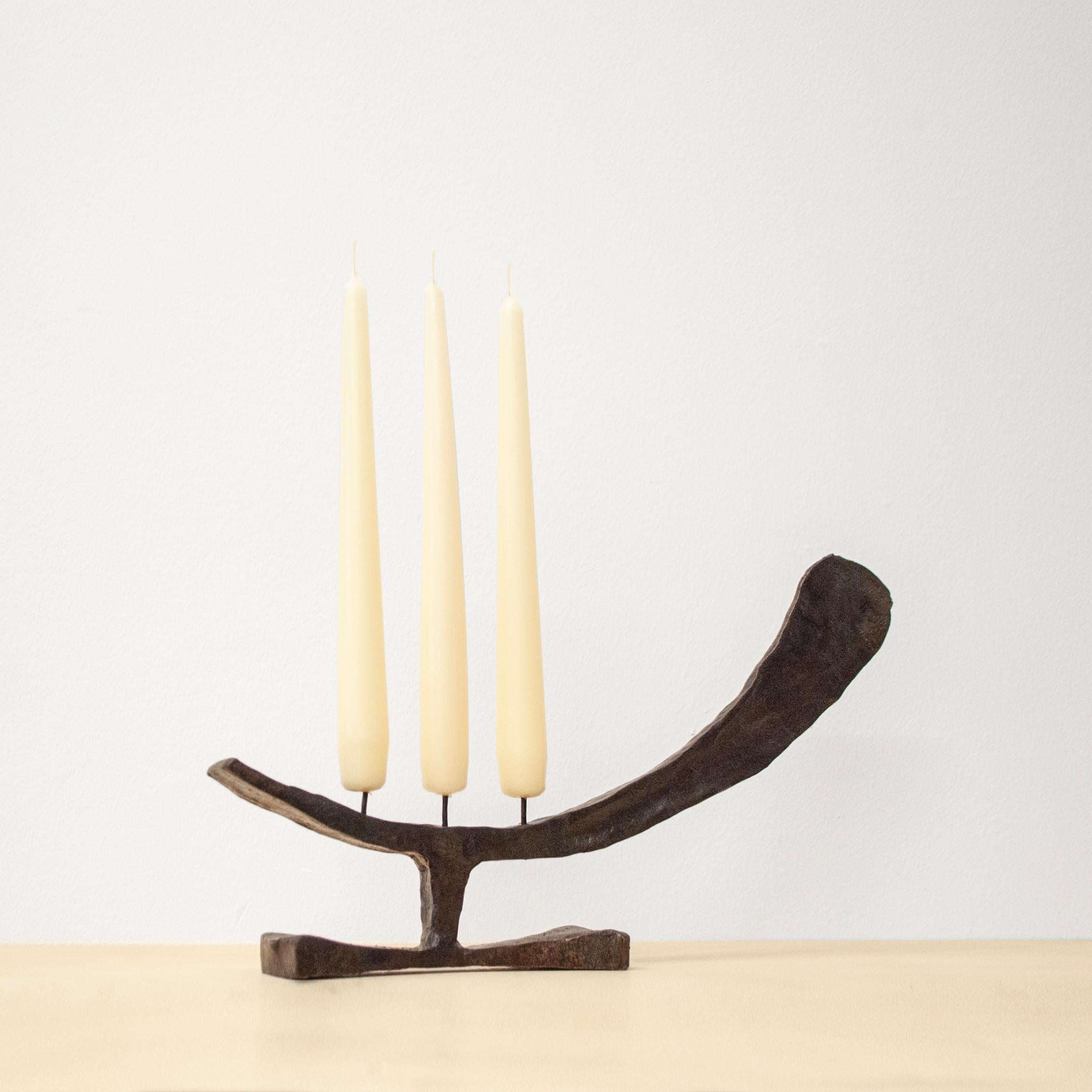 A forged steel candleholder inspired by Harry Bertoia. A tapered steel form sits horizontally, bowed and raised up on a base. The tapered form is forged from one piece of steel tapering in 2 directions to allow for an interesting profile and a flat