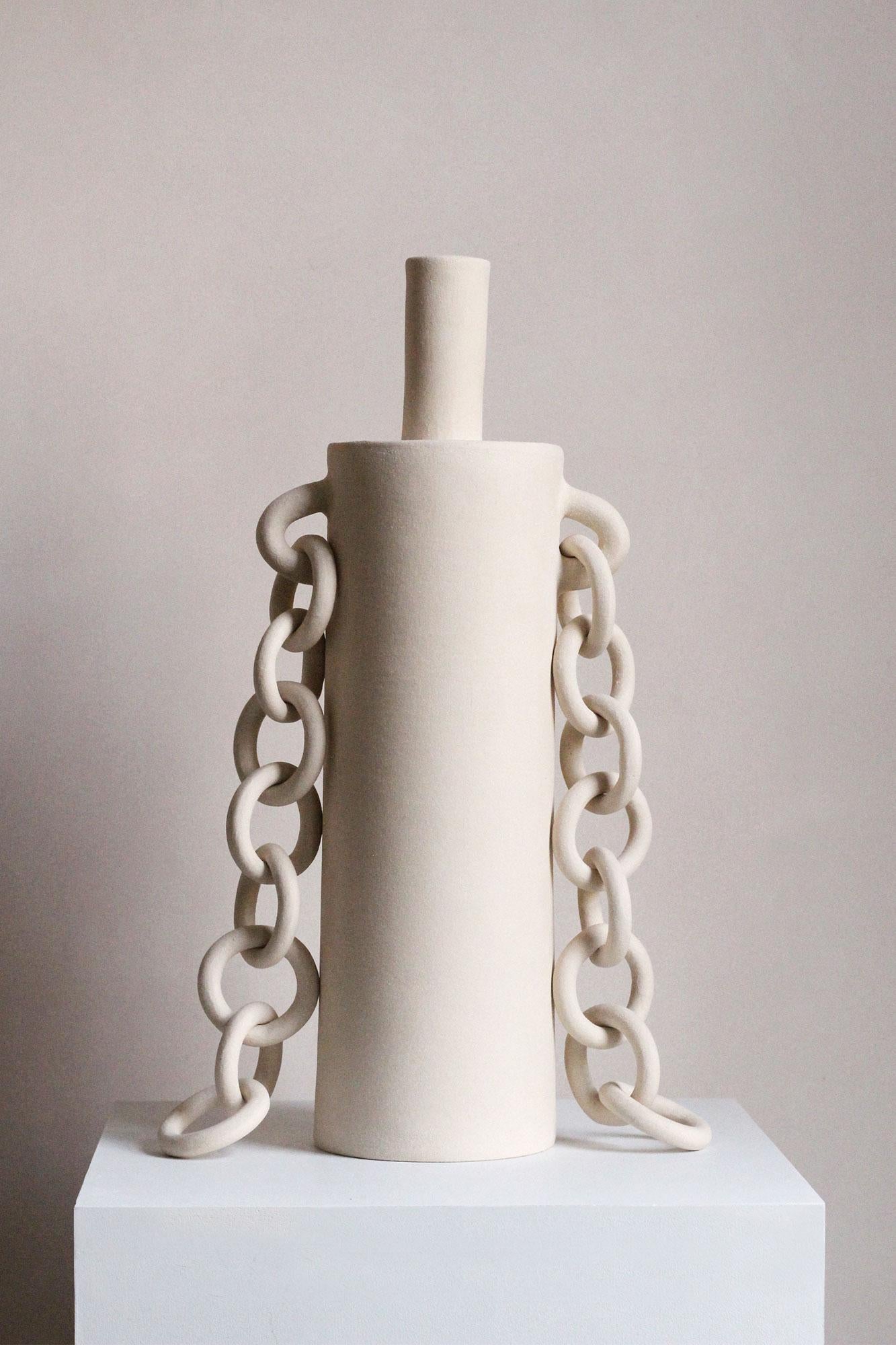 Hecha a mano en gres, esta escultura contemporánea presenta cadenas de cerámica que cuelgan a ambos lados de la escultura cilíndrica, adornando la forma como si fueran joyas. Creada por Miyelle en su estudio de Hackney, Londres, esta pieza única