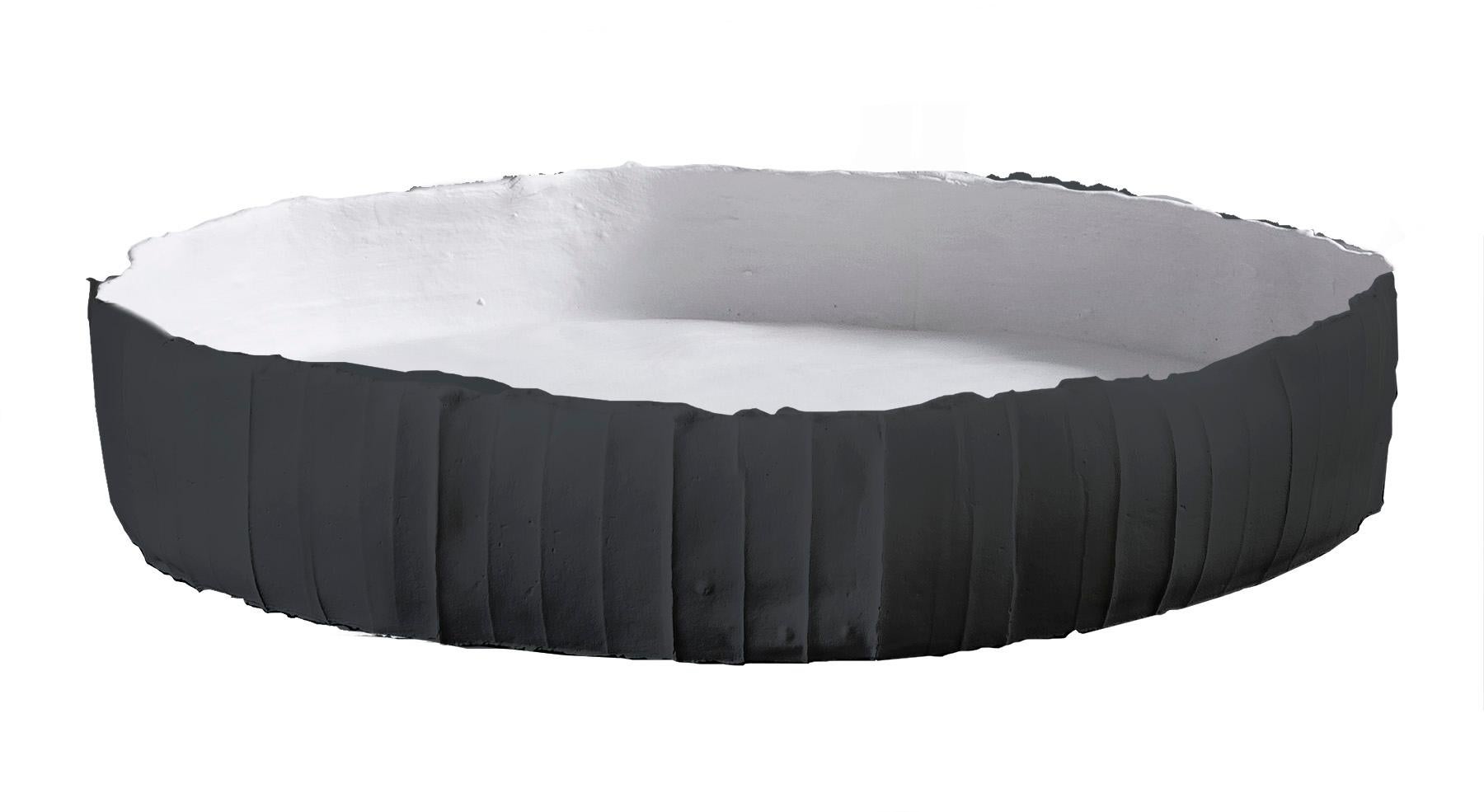 Un pezzo dal carattere forte e moderno, questo accattivante vassoio è stato realizzato a mano in paper clay (composto a base di argilla mescolato con fibre naturali); la forma circolare leggermente irregolare è rifinita con un interno bianco