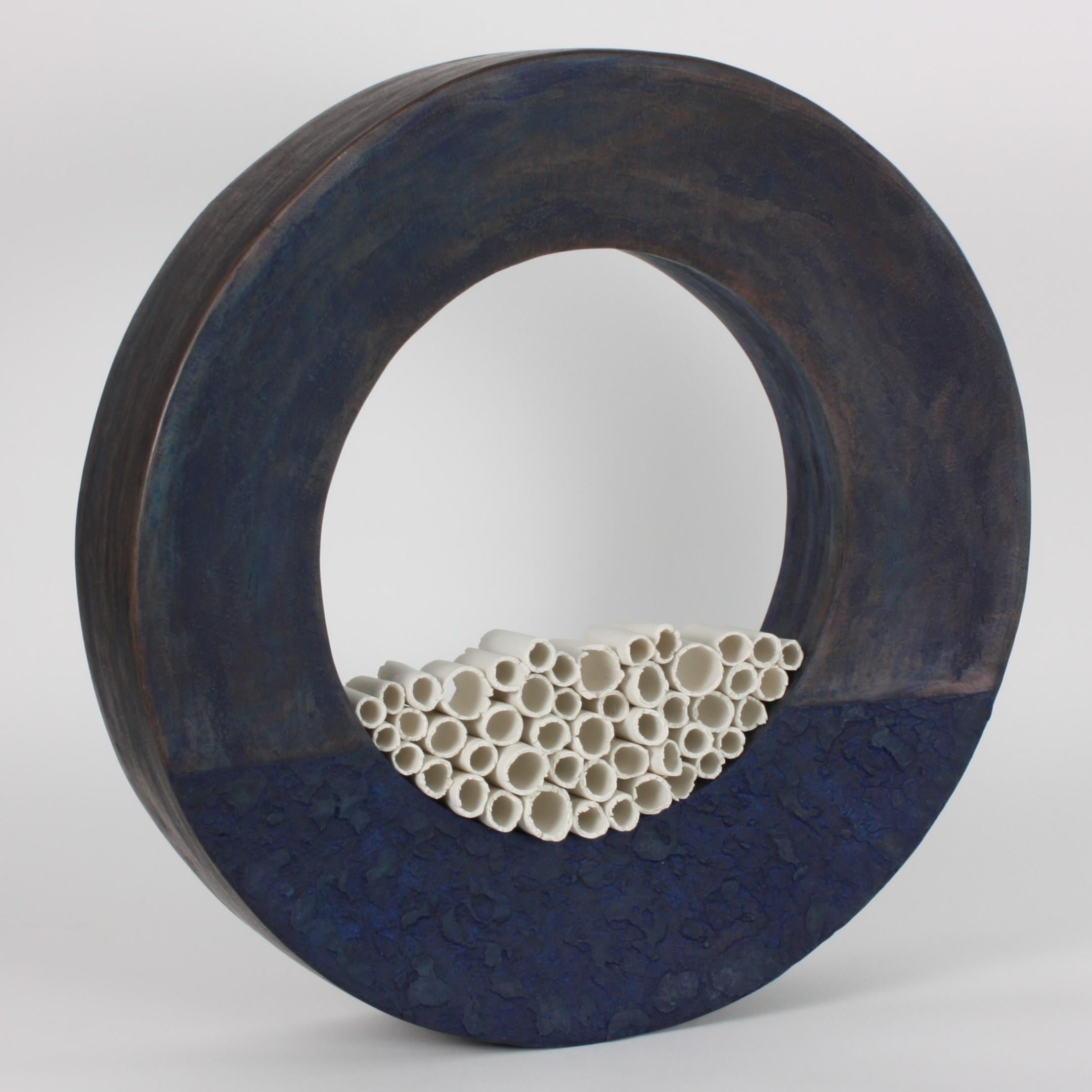 This contemporary blue ceramic ring sculpture in earthenware and porcelain is an exceptional piece. A composition of irregular silken porcelain tubes, suggestive of parchment or papyrus scrolls, are assembled inside a dark blue matte ring with rich
