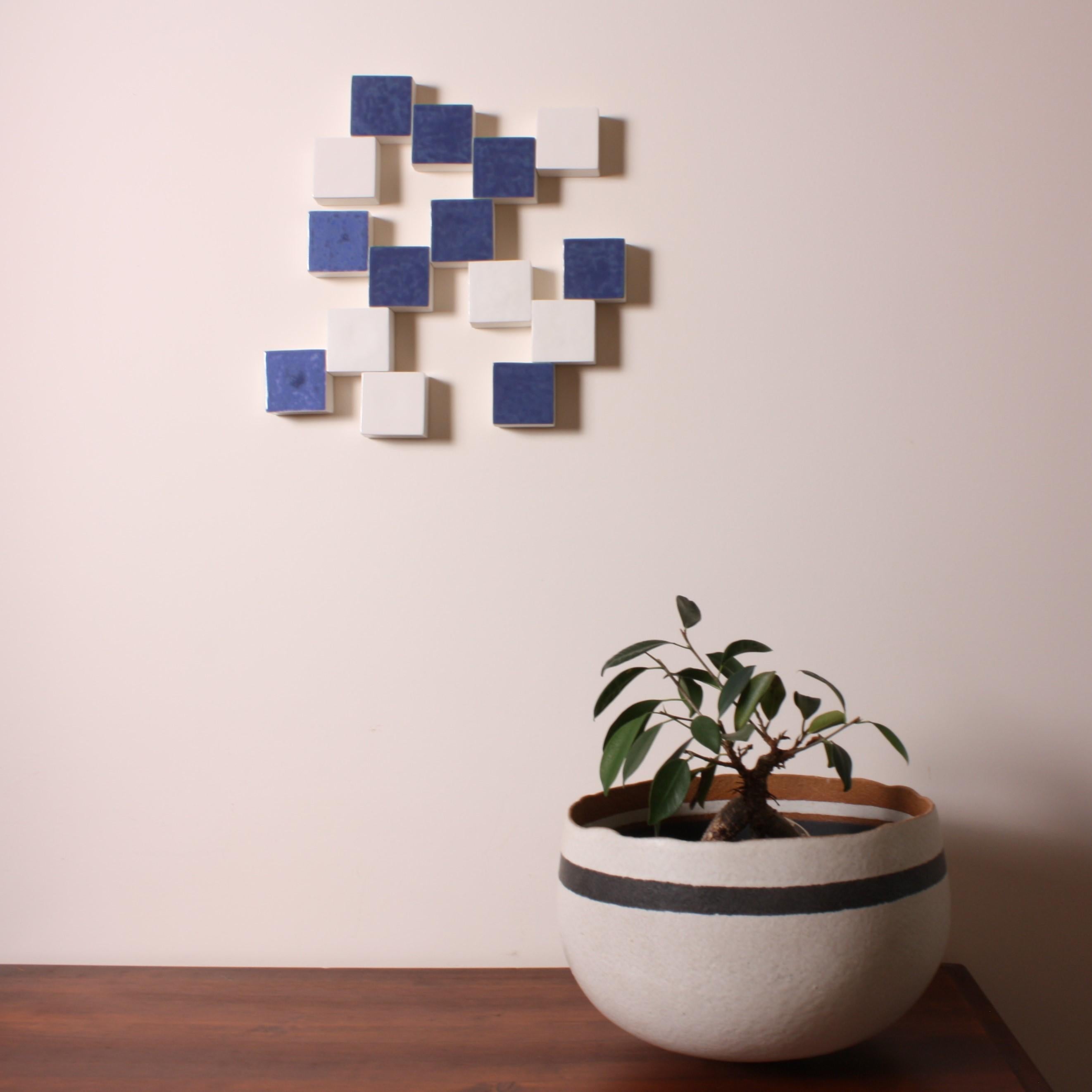 Composition of handmade blue and white cubic porcelain elements assembled into a unique wall mural. The various colors and textures of each surface, in porcelain matte or in glossy or satin enamel, make the piece