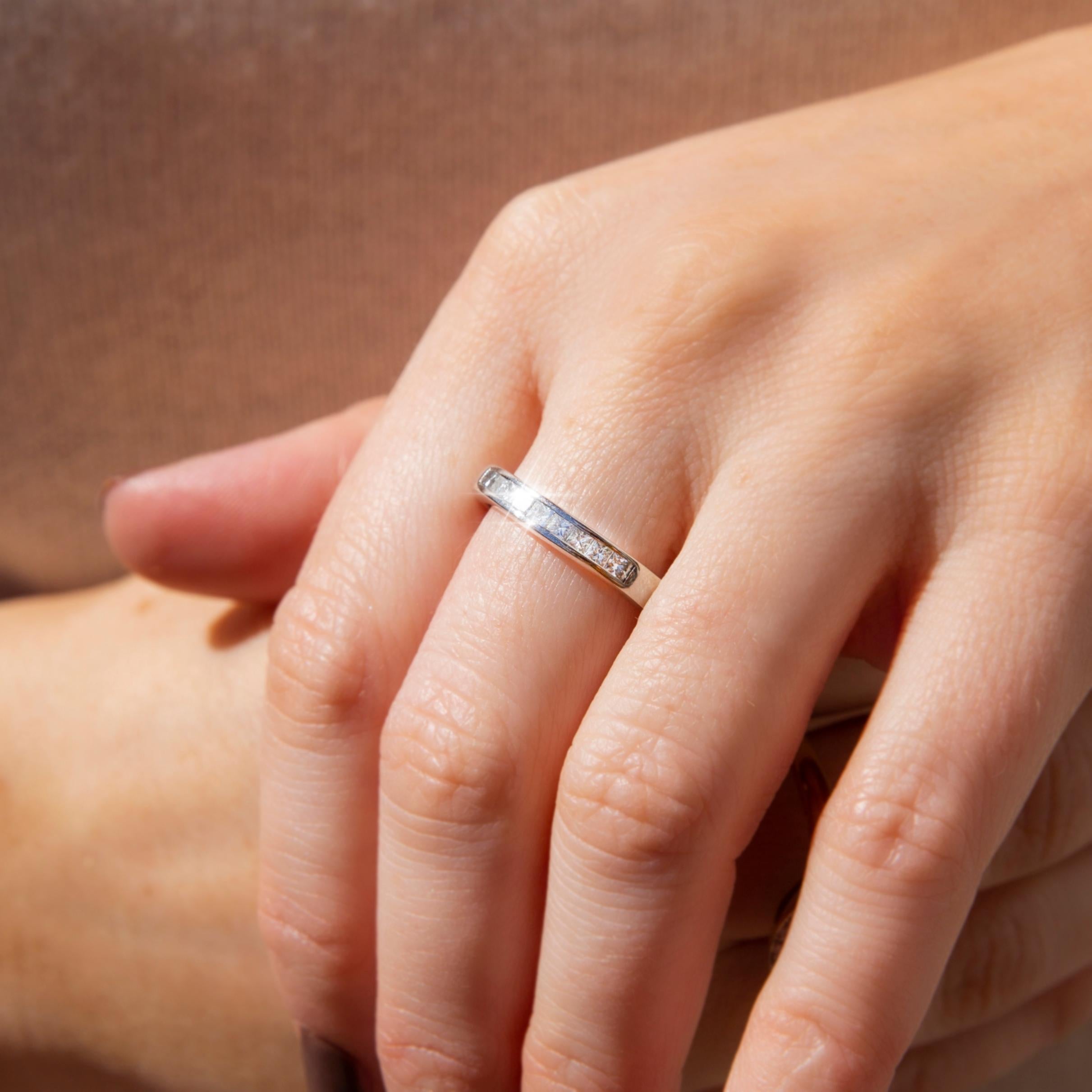Dieser schöne, moderne Ring ist aus Platin geschmiedet und zeichnet sich durch eine glitzernde Reihe von neun Diamanten im Prinzessinnenschliff aus, die sich auf der Vorderseite eines funkelnden weißen Bandes befinden. Wir haben diese