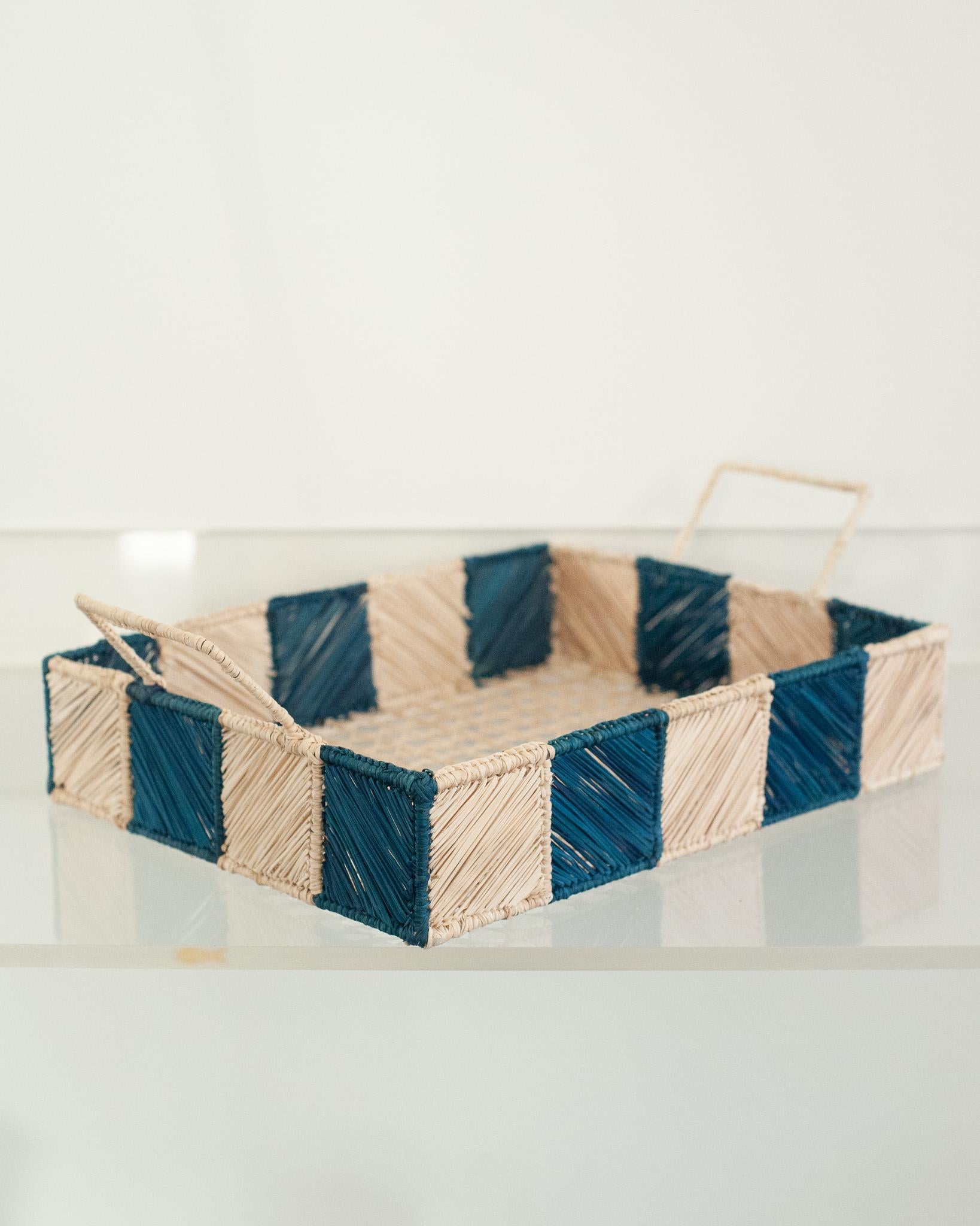 Uplift your table with this stunning handwoven rattan tray with blue and natural checkered sides and handles. Finely crafted by expert artisans, this piece showcases the classical technique of weaving in a modern way. From Jean Michel Frank to the