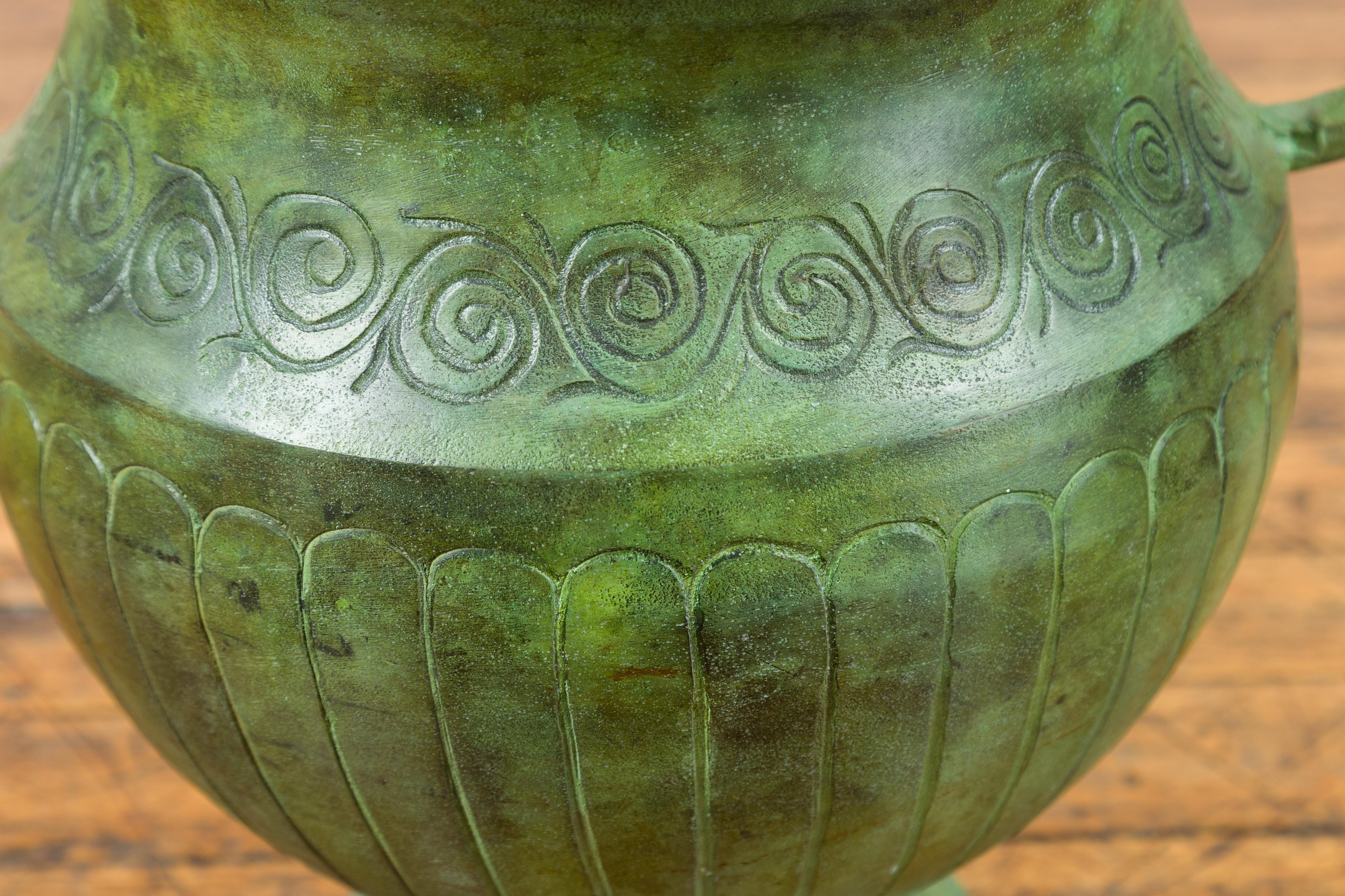 A contemporary classical style urn with Verde patina, large handles and gadroon motifs. Created in a classical style, this urn is adorned with a frieze of meanders sitting above a gadrooned belly. It is the sides however that attract our attention