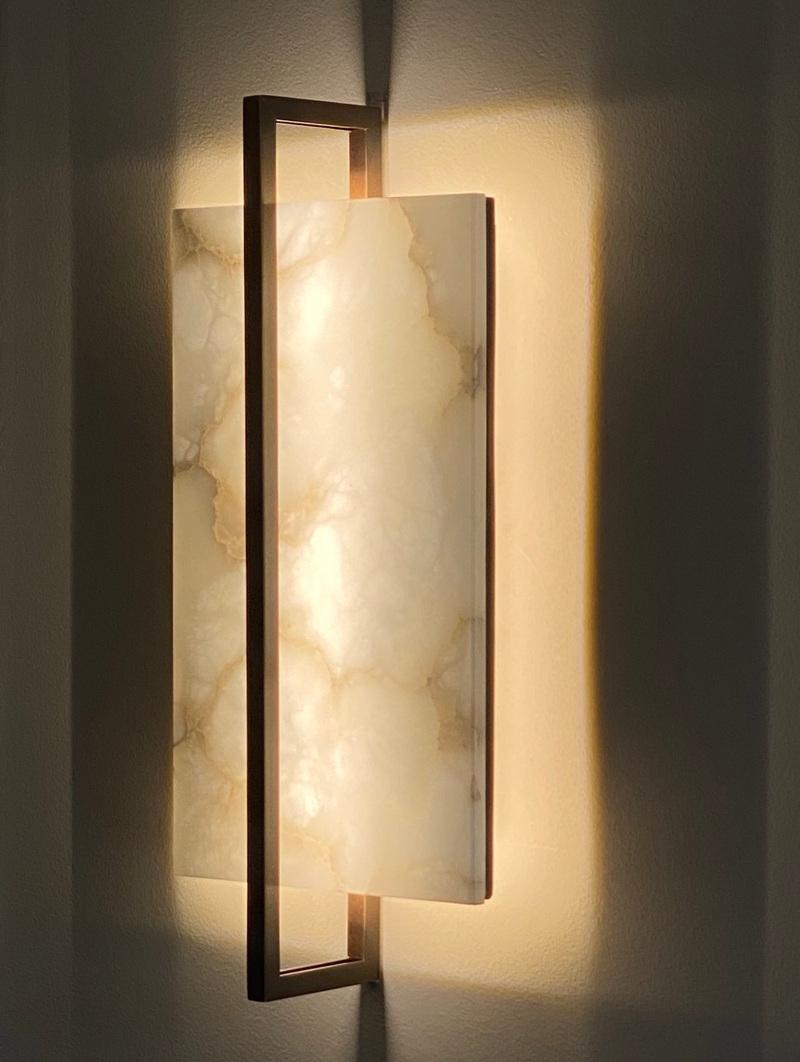 The Tile wall light, with its clean and simple lines, has a very contemporary flavor that is in strong contrast with the more traditional materials that make it up, such as veined alabaster and light bronze. The two levels of warm white led light
