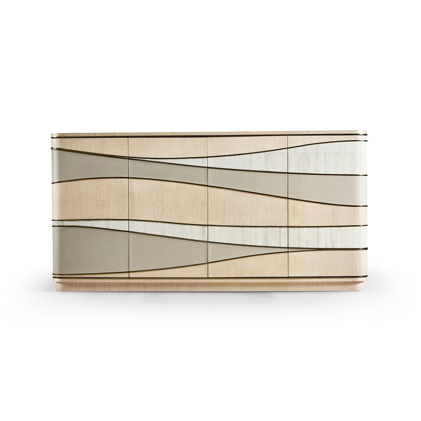 Its flowing wave motif, created with crème leather, natural bone inlay, and light wood, exudes a refined coastal elegance. Delicate metal inlays in a satin brass finish add a subtle glimmer, highlighting its sculptural design. This sideboard