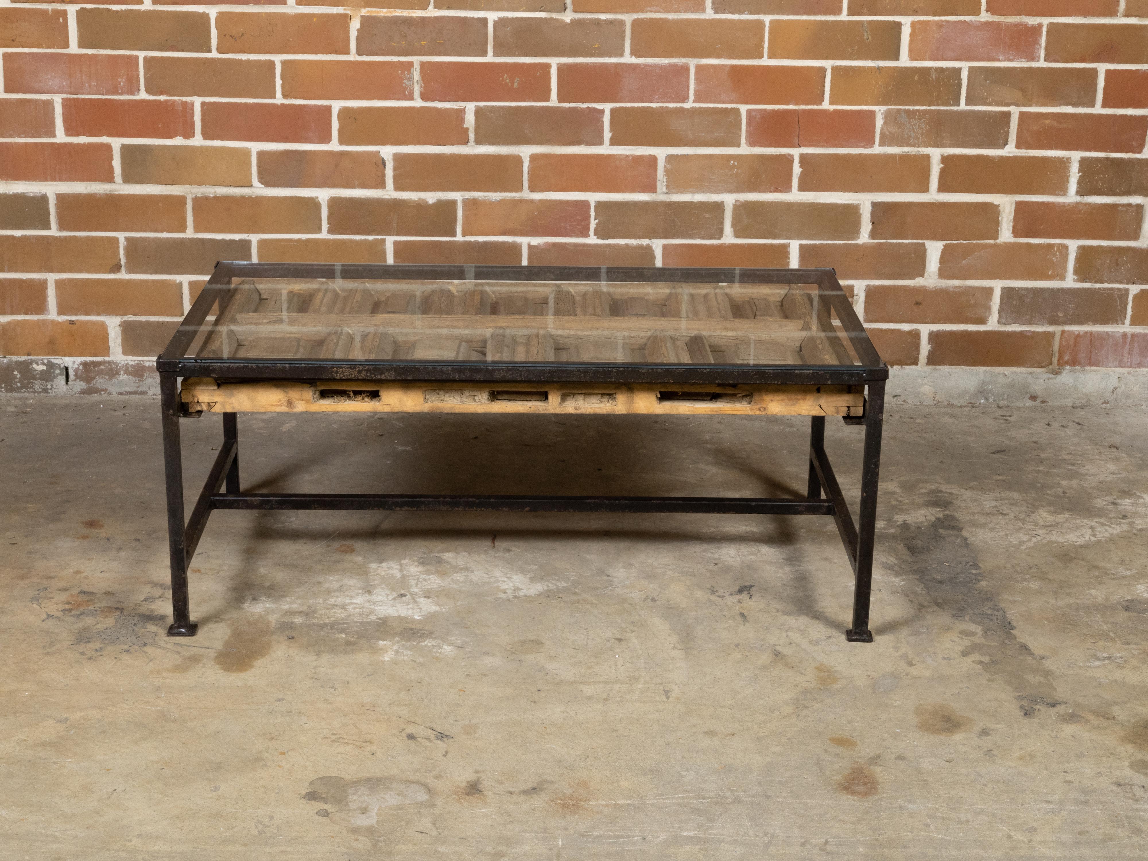 A contemporary coffee table made from an antique wooden fragment door with raised motifs under glass and mounted on a custom black iron base. Newly made in the USA, this coffee table features a beautifully rustic rectangular top made from an antique