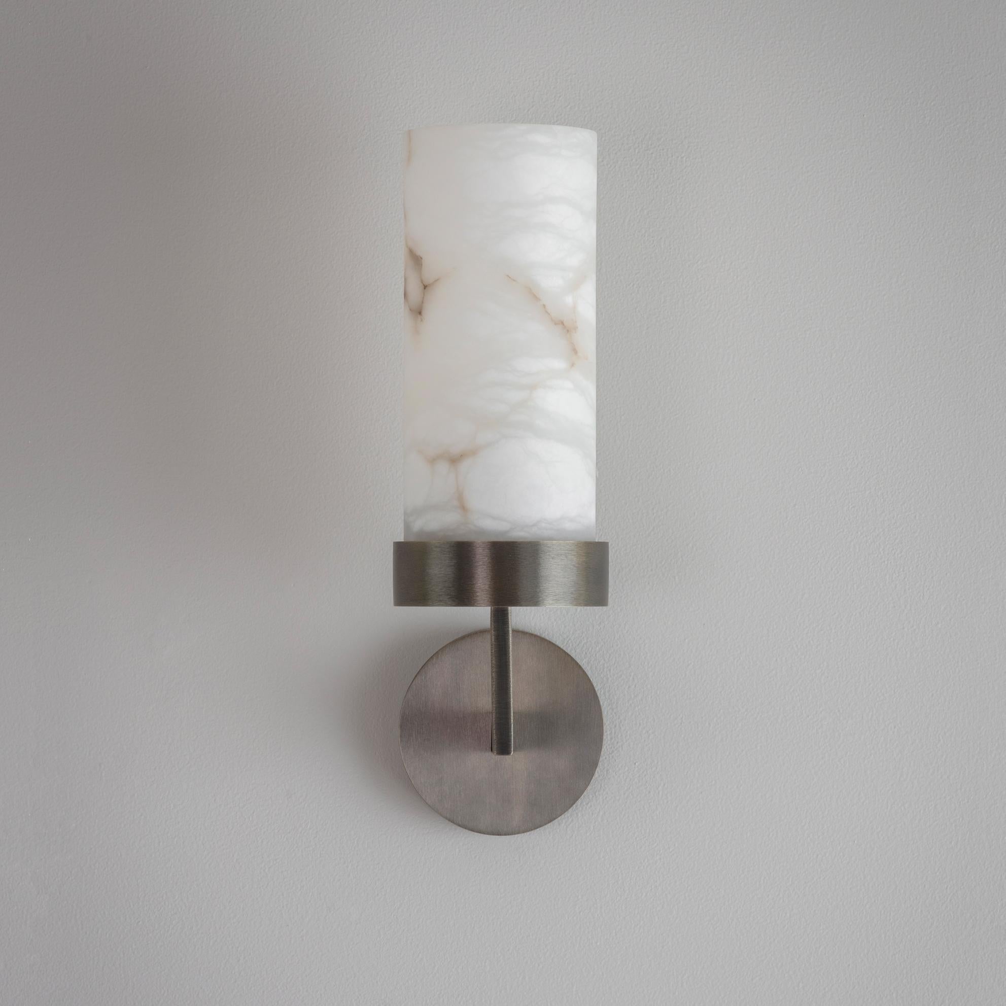 An elegant wall light featuring shades hewn from solid alabaster. The soft opalescent alabaster shade is offset by the clean contemporary lines of the hand-grained metalwork. When lit, the alabaster shade offers a stunning diffused light and