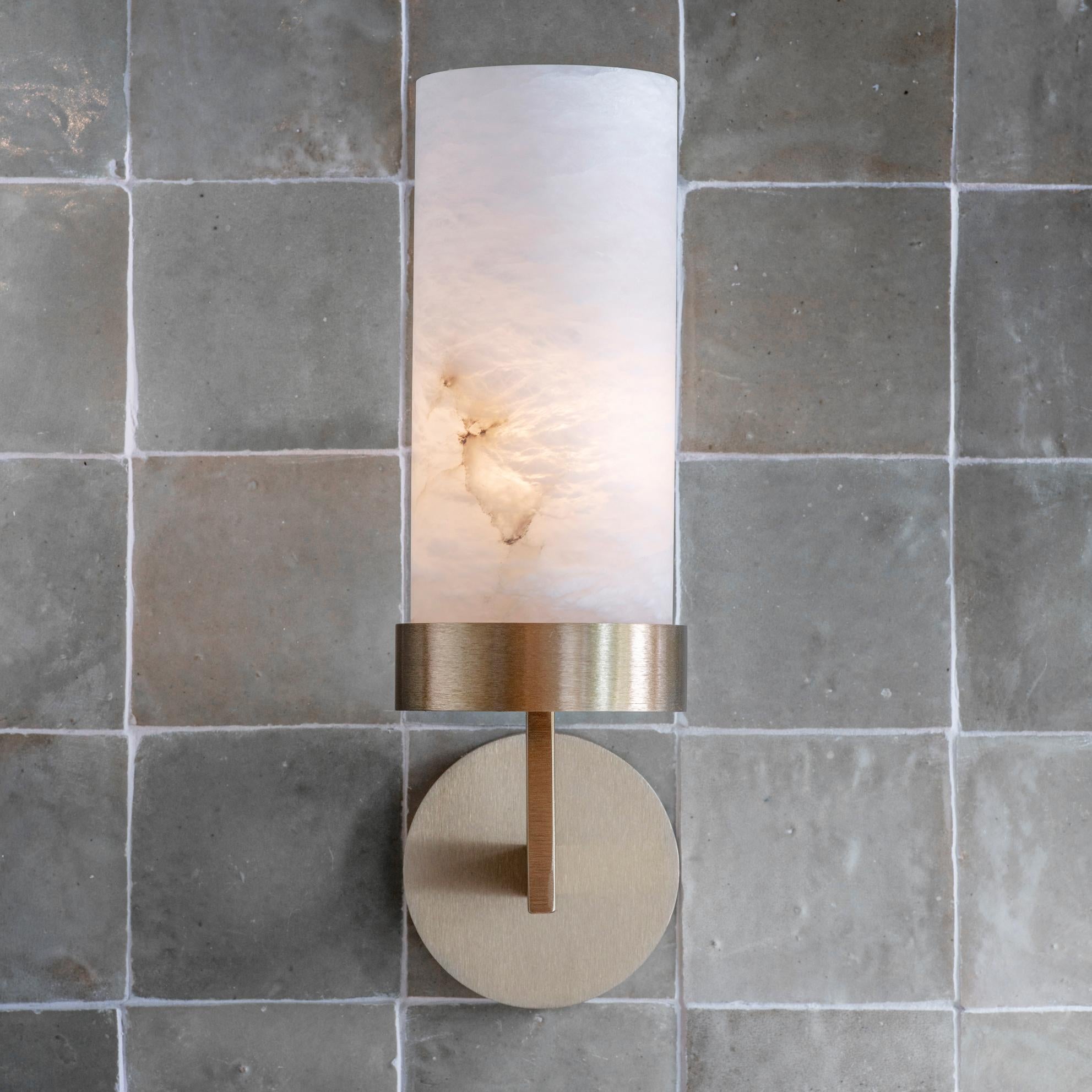 An elegant wall light featuring shades hewn from solid alabaster. The soft opalescent alabaster shade is offset by the clean contemporary lines of the hand-grained metalwork. When lit, the alabaster shade offers a stunning diffused light and