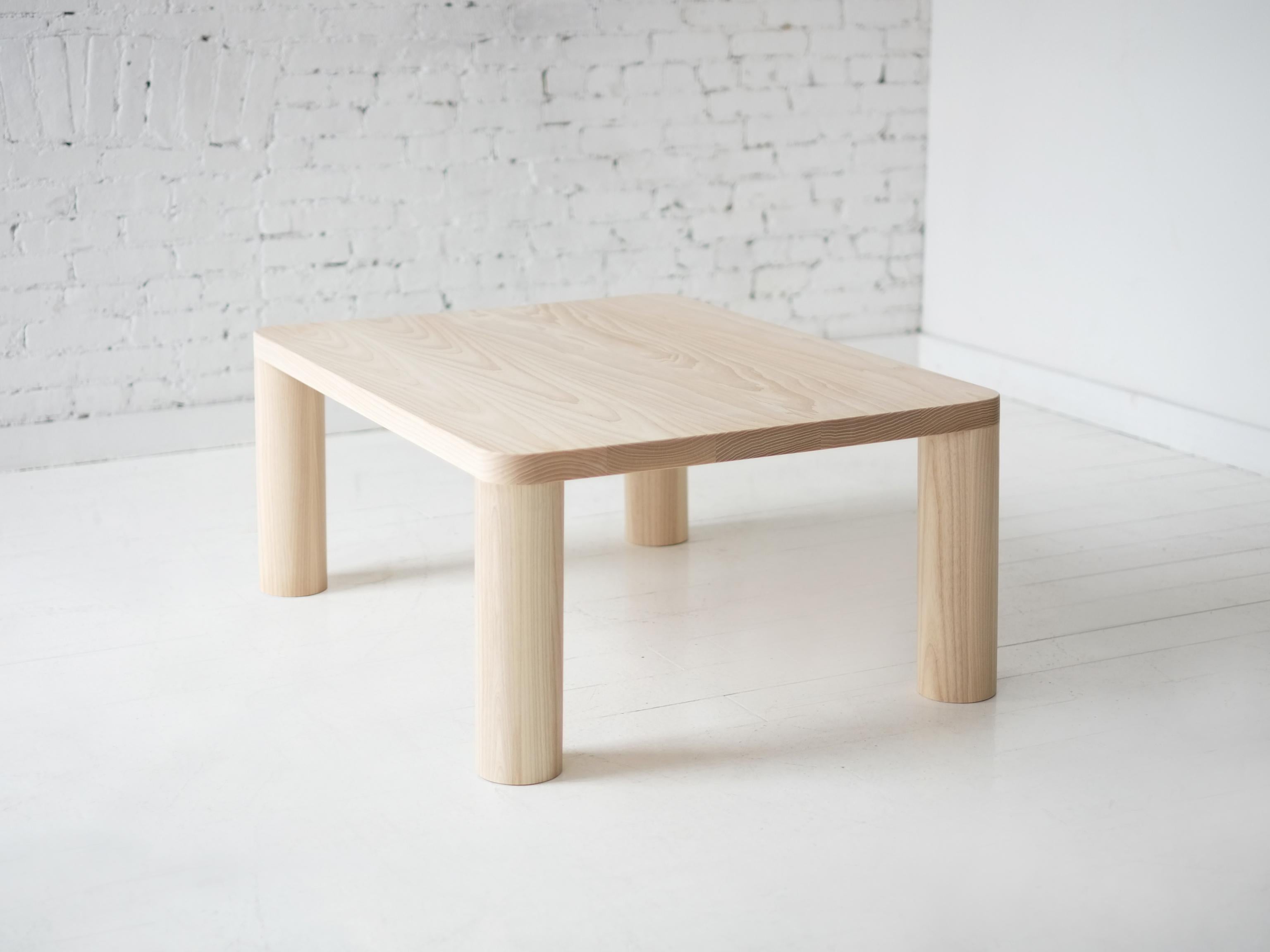This contemporary, minimal wooden coffee table features four large round legs that seamlessly meet and define the radii of the top, a quiet but powerful detail. 

Made to order in custom sizes, shapes, materials and finishes. Ash version pictured