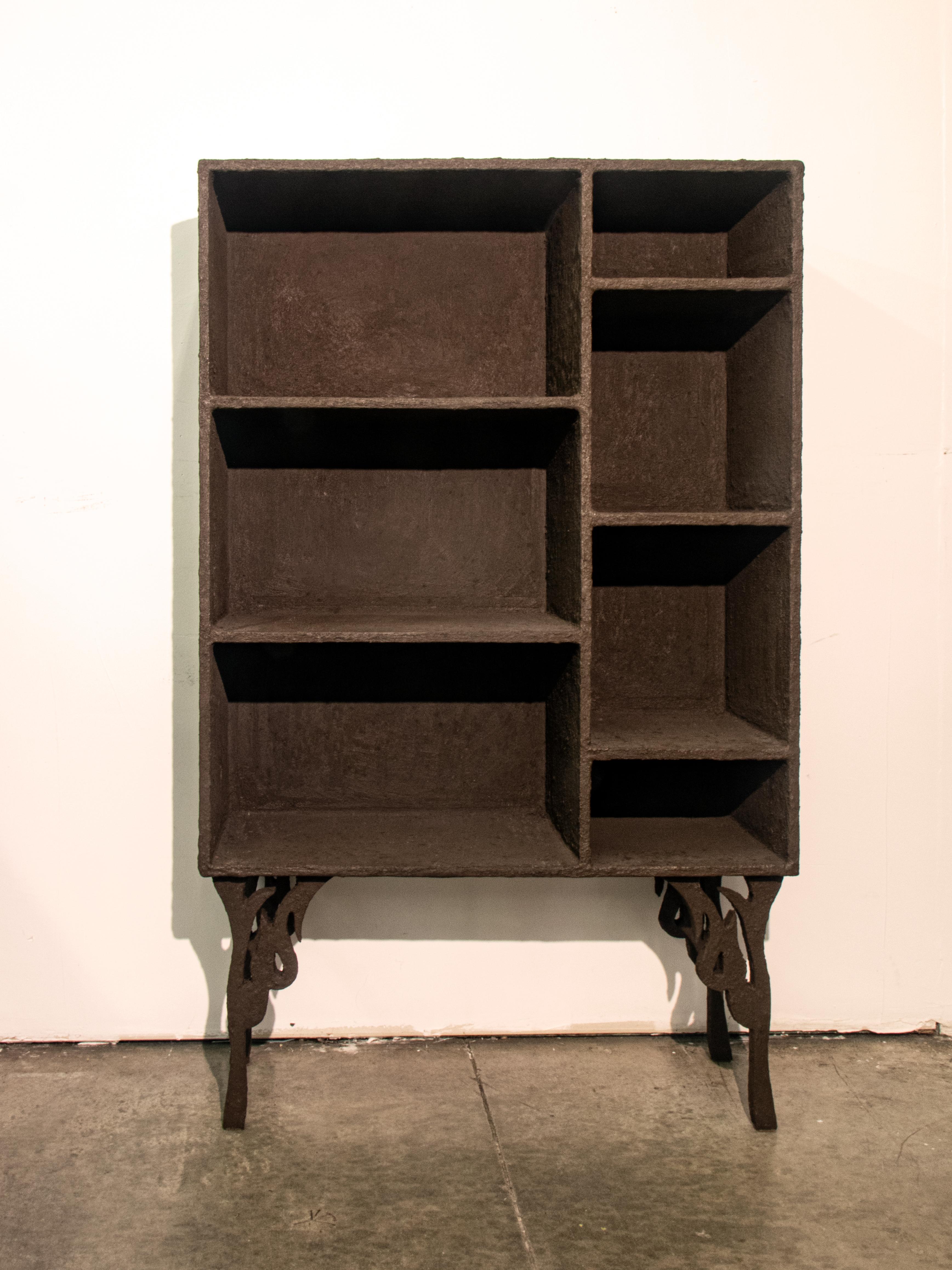 This handmade unique bookcase combines a wooden skeleton with a brown pigmented cement coat. The irregularity of the texture unique to this piece give the bookshelf a rough and spontaneous finish, with the flame shaped legs adding an element of
