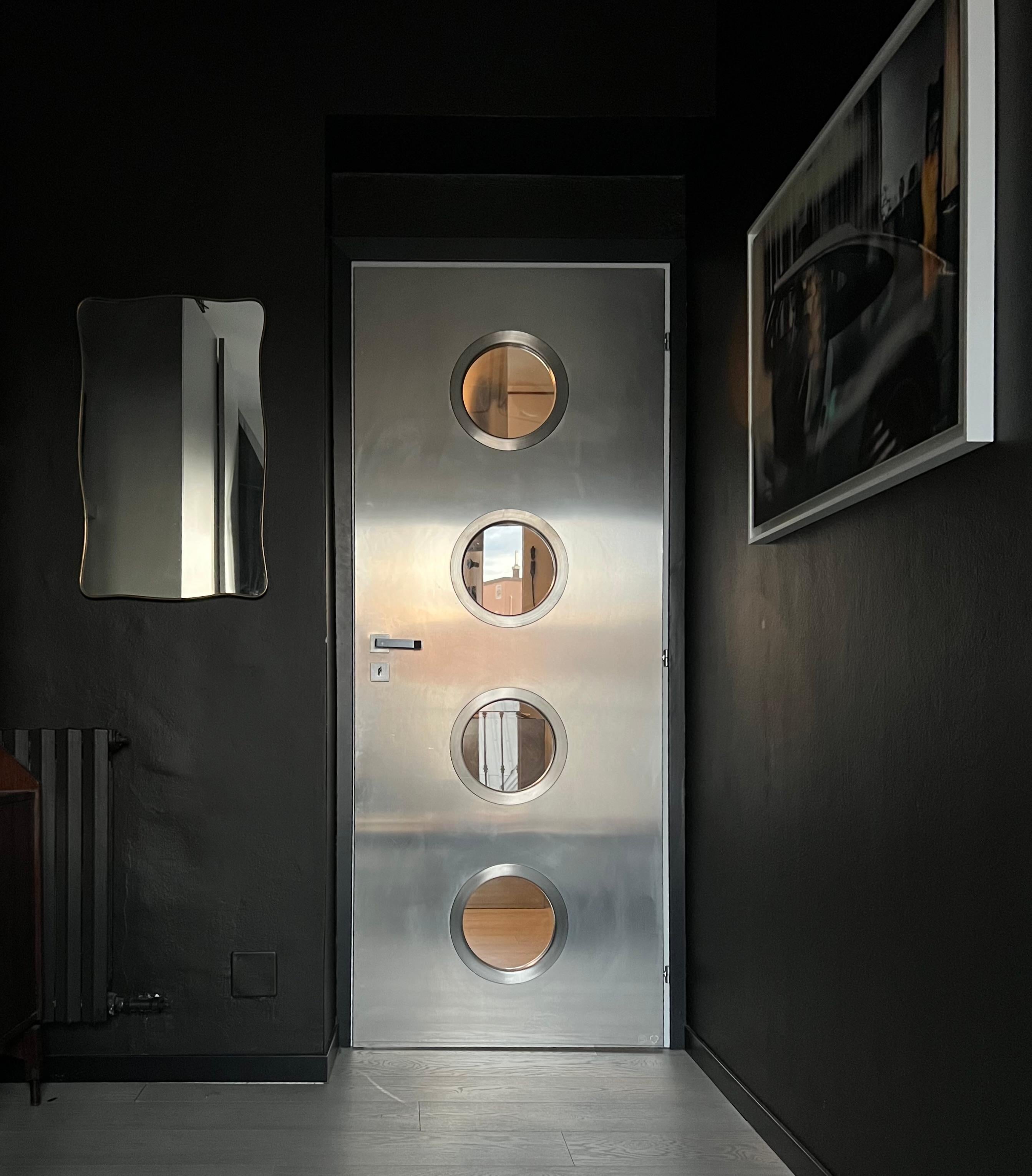 Porte métallique contemporaine sur mesure en acier inoxydable avec hublots ronds, conçue par Spinzi et fabriquée en Italie.

Inspirée par les œuvres de Jean Prouvé, cette porte est construite autour d'une porte en bois ordinaire existante, avec