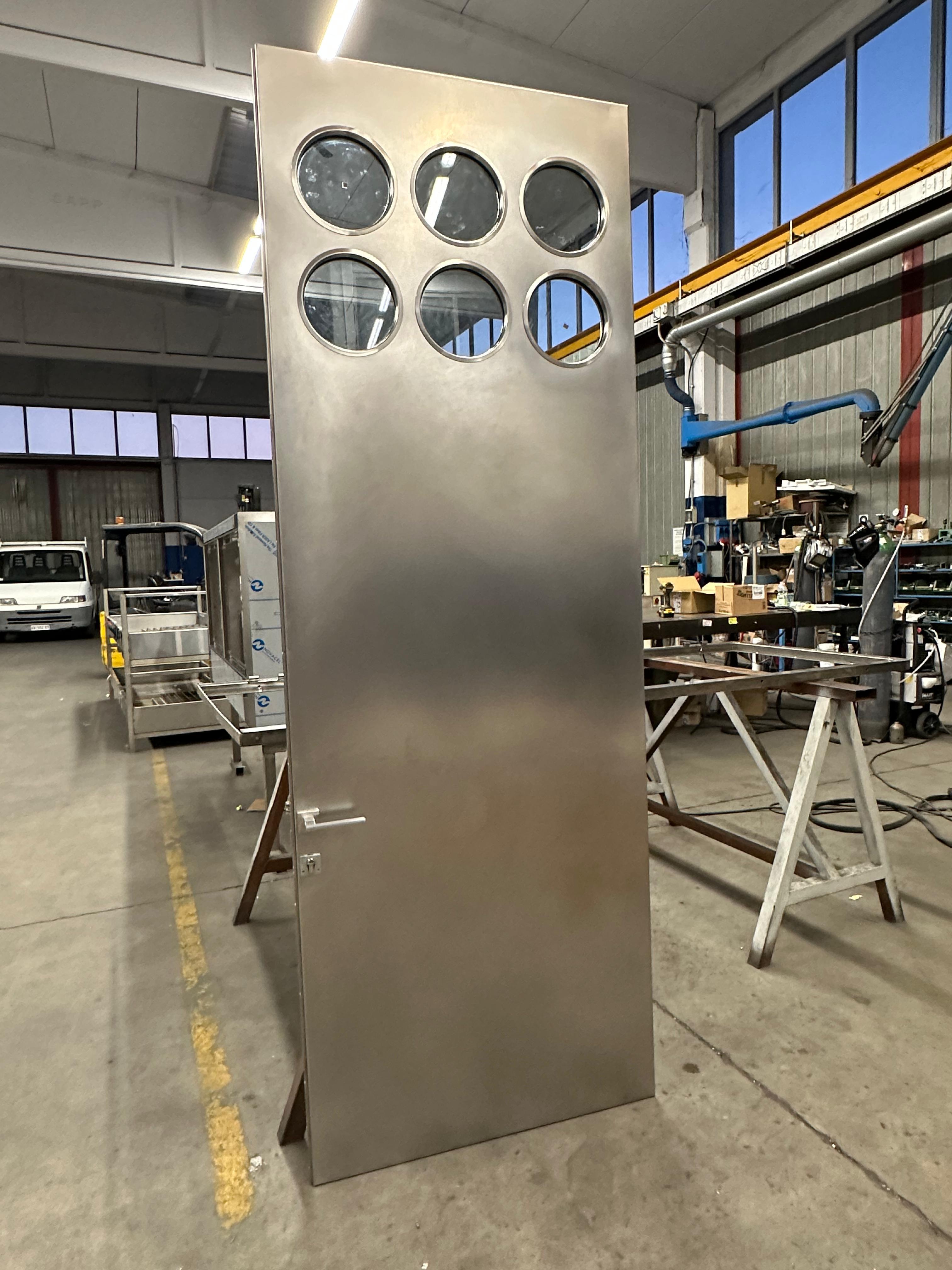 Contemporary custom made stainless steel metal door with round portholes, designed by Spinzi and made in Milano.

Inspired by the works of Jean Prouvé, Portaluppi and the designers/artist of that era , this door is built around an existing regular
