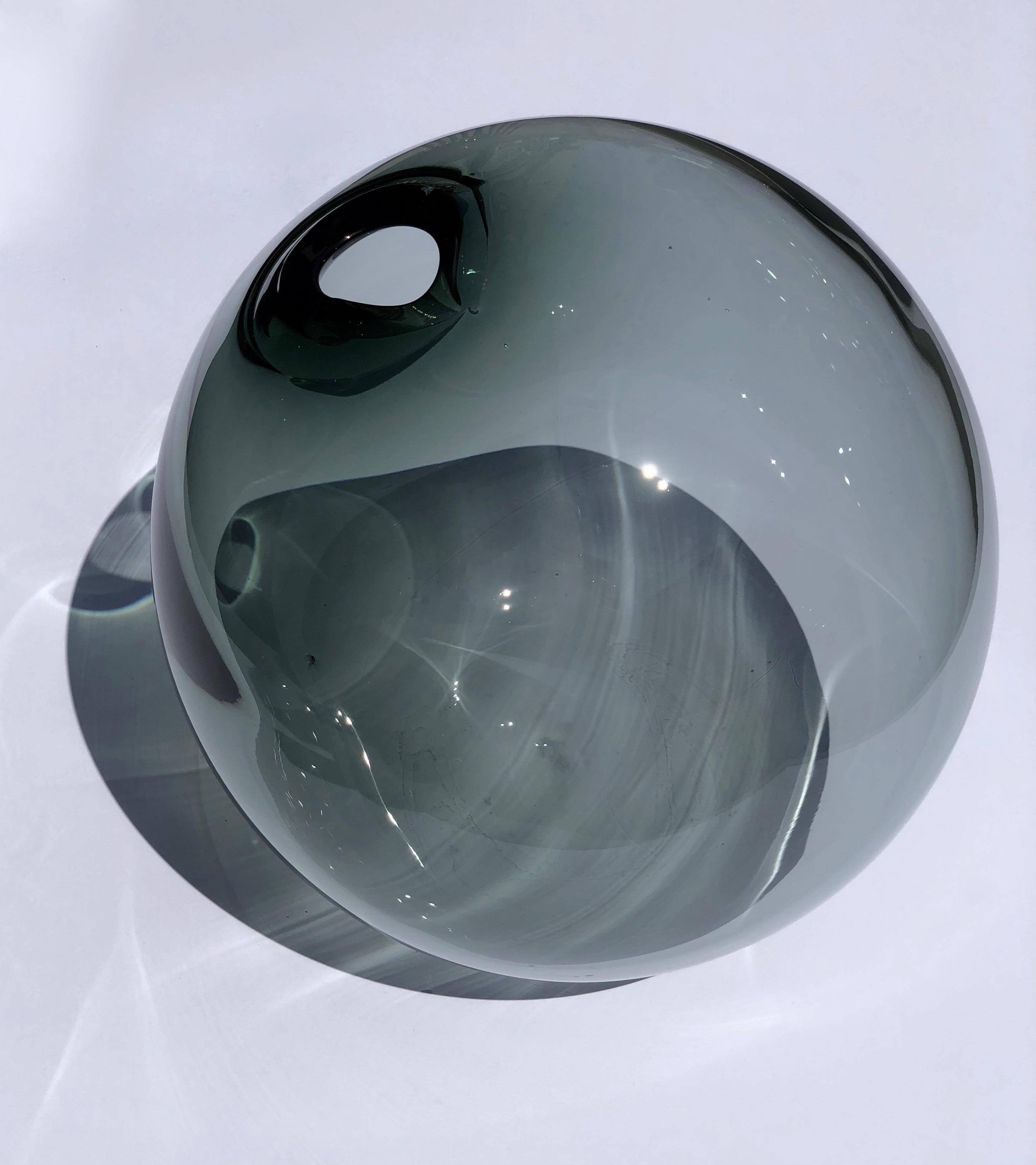 A beautiful, round glass vase, that has been hand blown into an organic form. Smoky grey in color and 30 mm
in diameter. The size and transparent color give it a feeling of a bubble. The effect is heightened by placing the object in sun