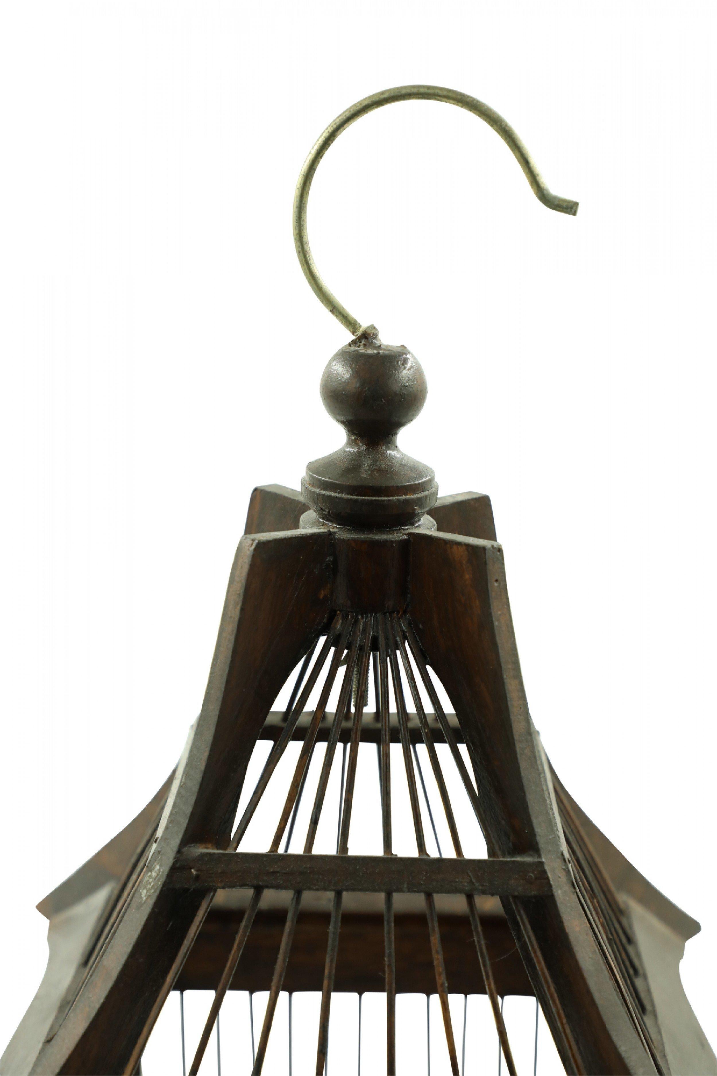 Contemporary wooden birdcage with a sloped roof, hanging hook, and two removable bottom trays with a dark brown stained finish.