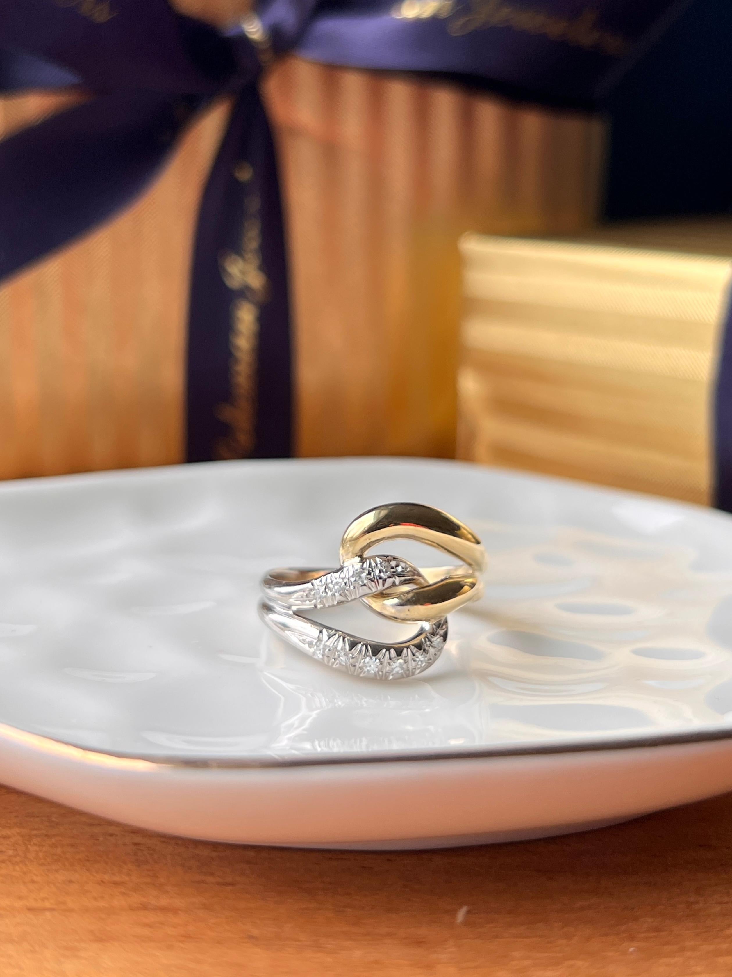 This contemporary 18K yellow and white gold ring features an elegant knotted design that blends modern styling with classic symbolism. The intertwining gold forms are accented by ten round single-cut diamonds totaling approximately 0.13 carats,