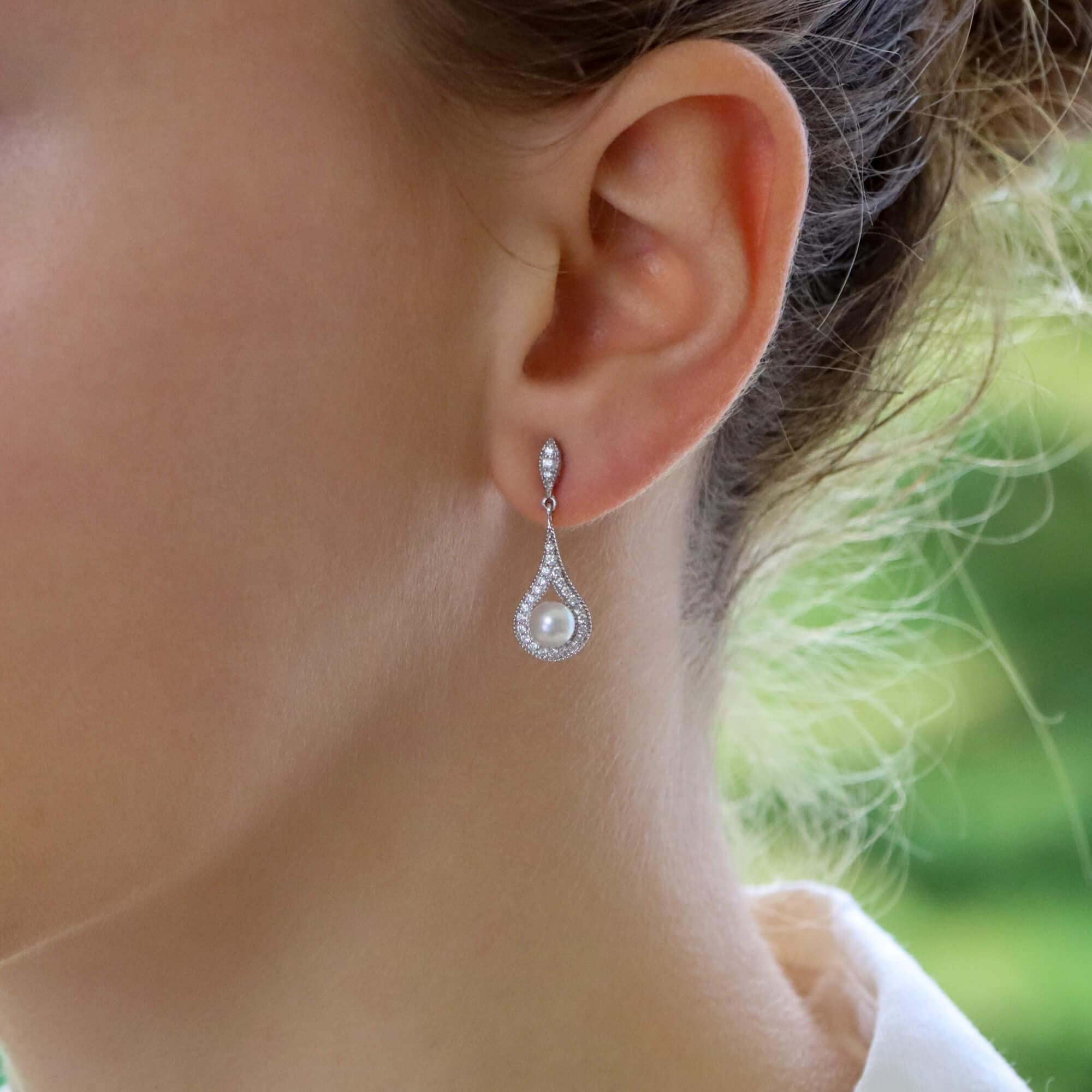 A beautiful pair of diamond and pearl drop earrings set in 18k white gold.

Each earring is composed of simple circular drop set centrally with a lustrous cream cultured pearl. The earrings are secured to reverse with a post and butterfly fitting.