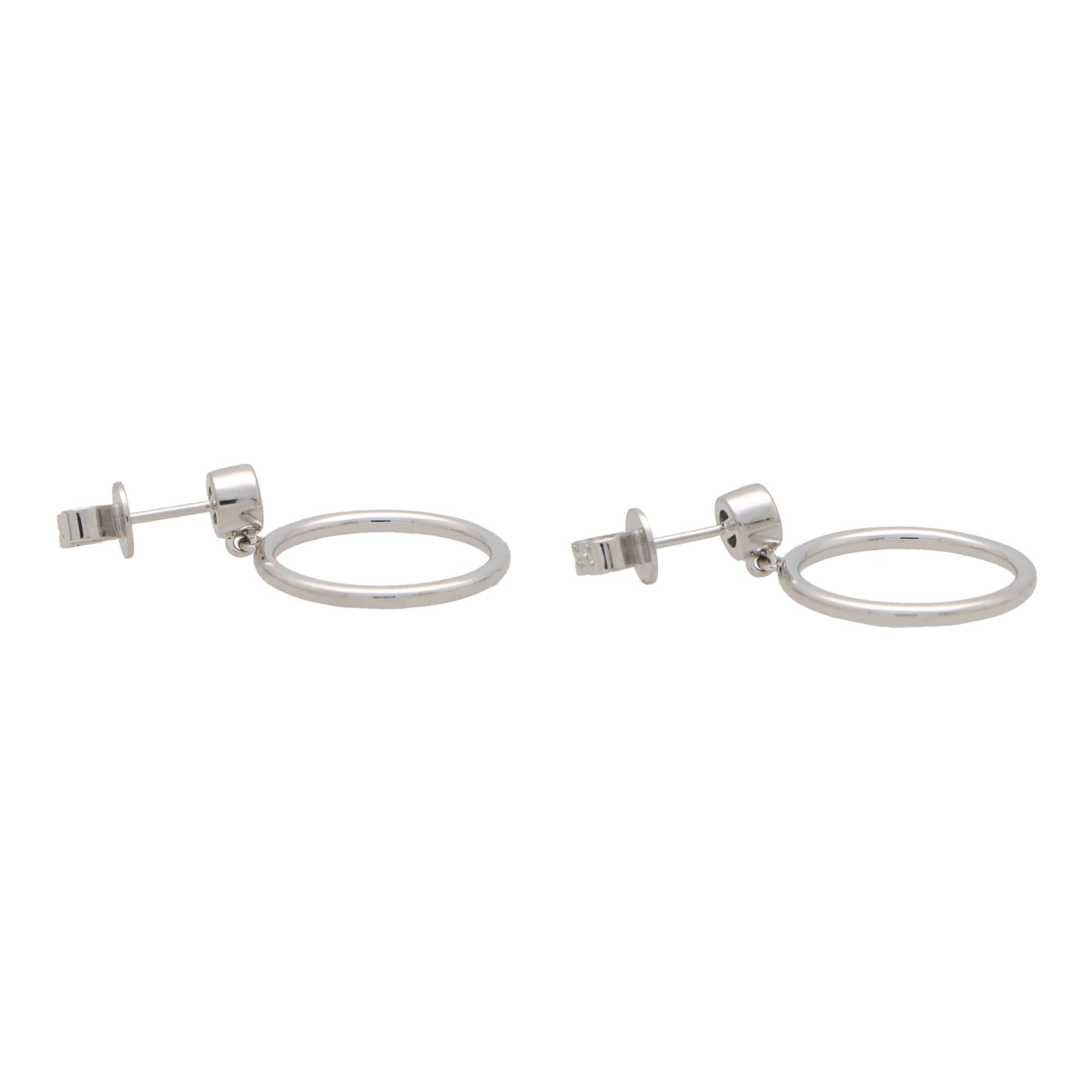 A stylish pair of contemporary diamond circle drop earrings set in 14k white gold.

Each earring features a rub over set round brilliant cut diamond which is secured with a post and butterfly fitting. Hanging freely from this stud is a solid