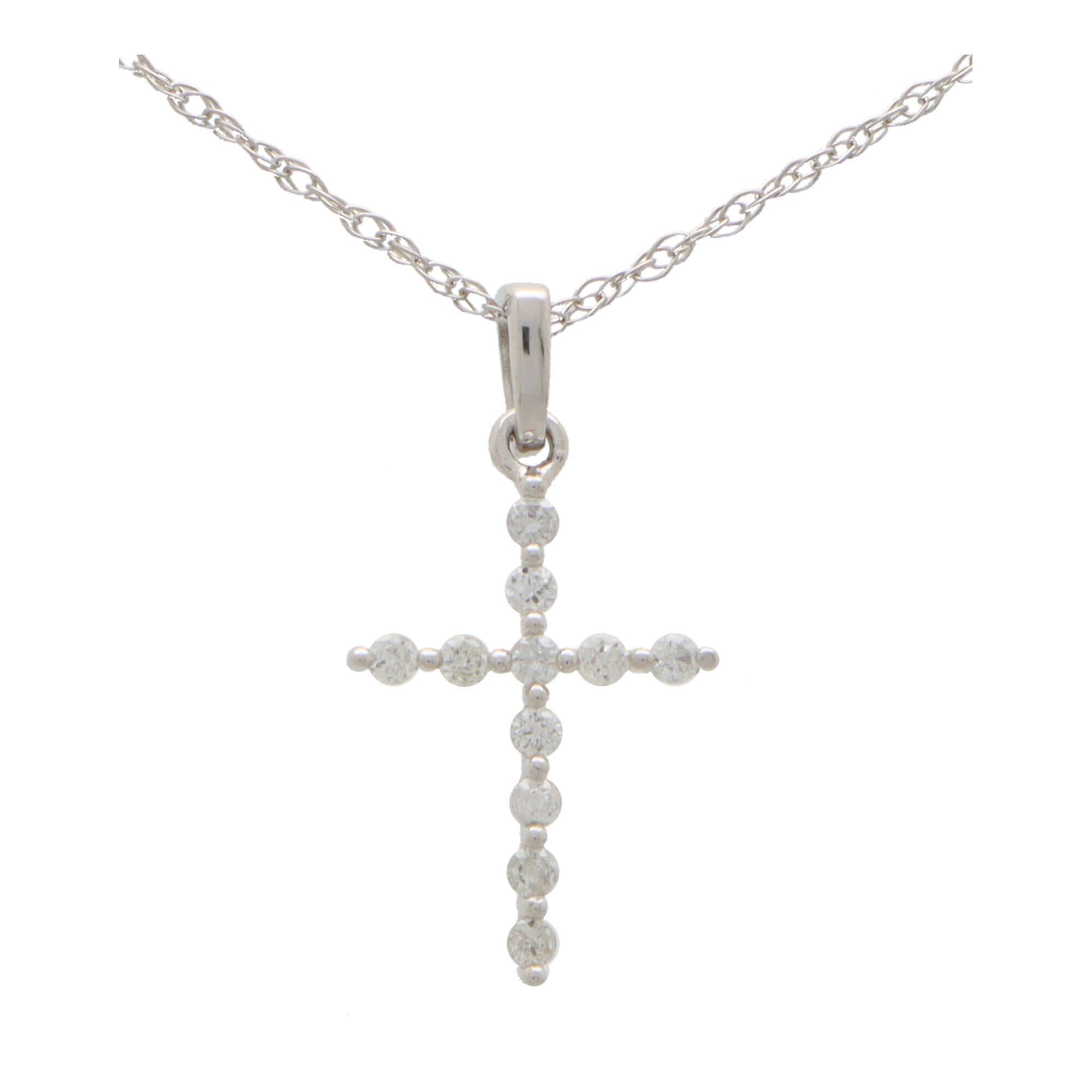A dainty diamond cross pendant necklace set in 14k white gold.

The pendant depicts a cross motif and is claw set with exactly 11 round brilliant cut diamonds. The cross hangs from a white gold bail and hangs from a fine 18-inch white gold trace
