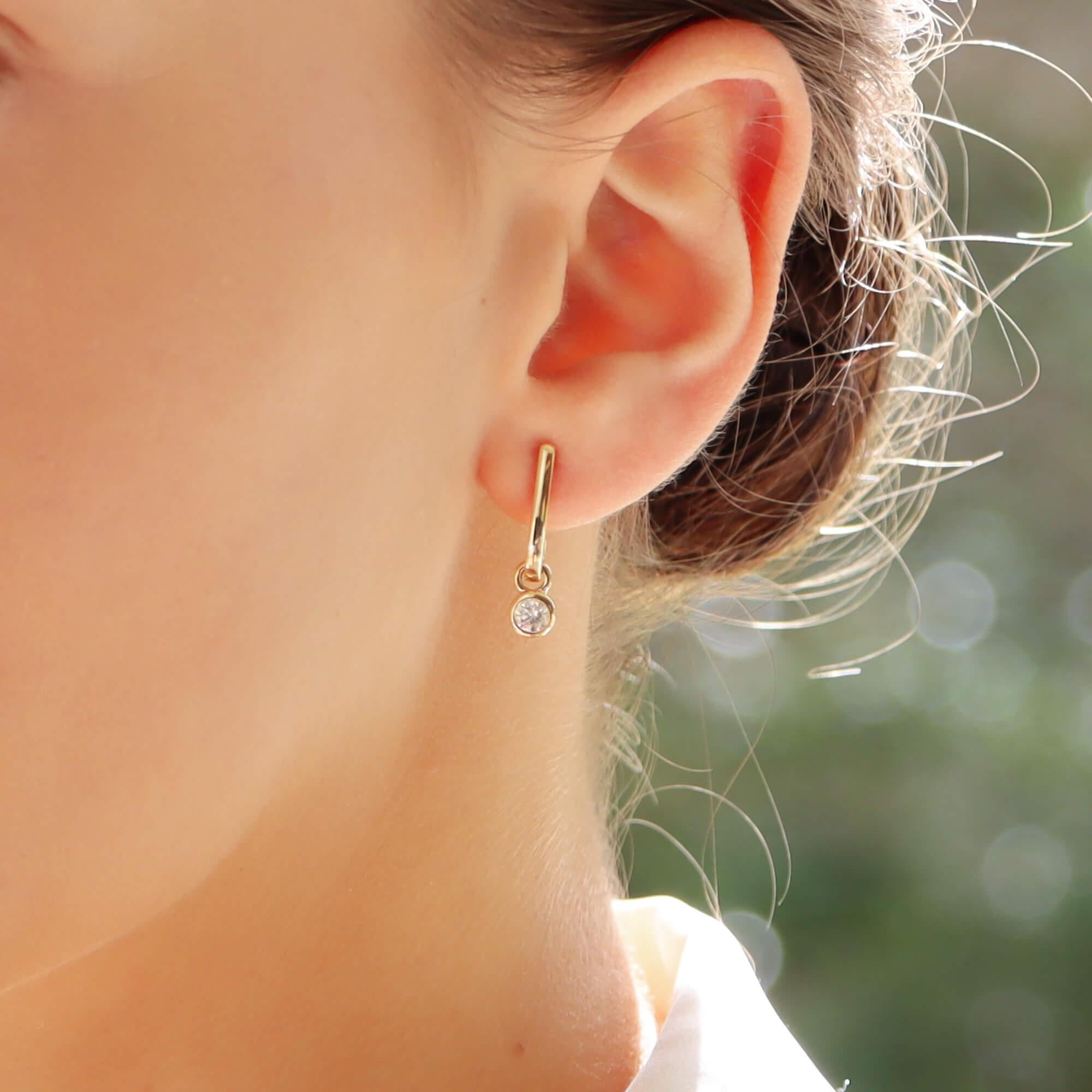 A perfect everyday pair of diamond drop half hoop earrings set in 14k yellow gold.

The earrings are composed of a solid gold half hoop from which hangs a rub over set round brilliant cut diamond. The diamond hangs freely and sparkles from all