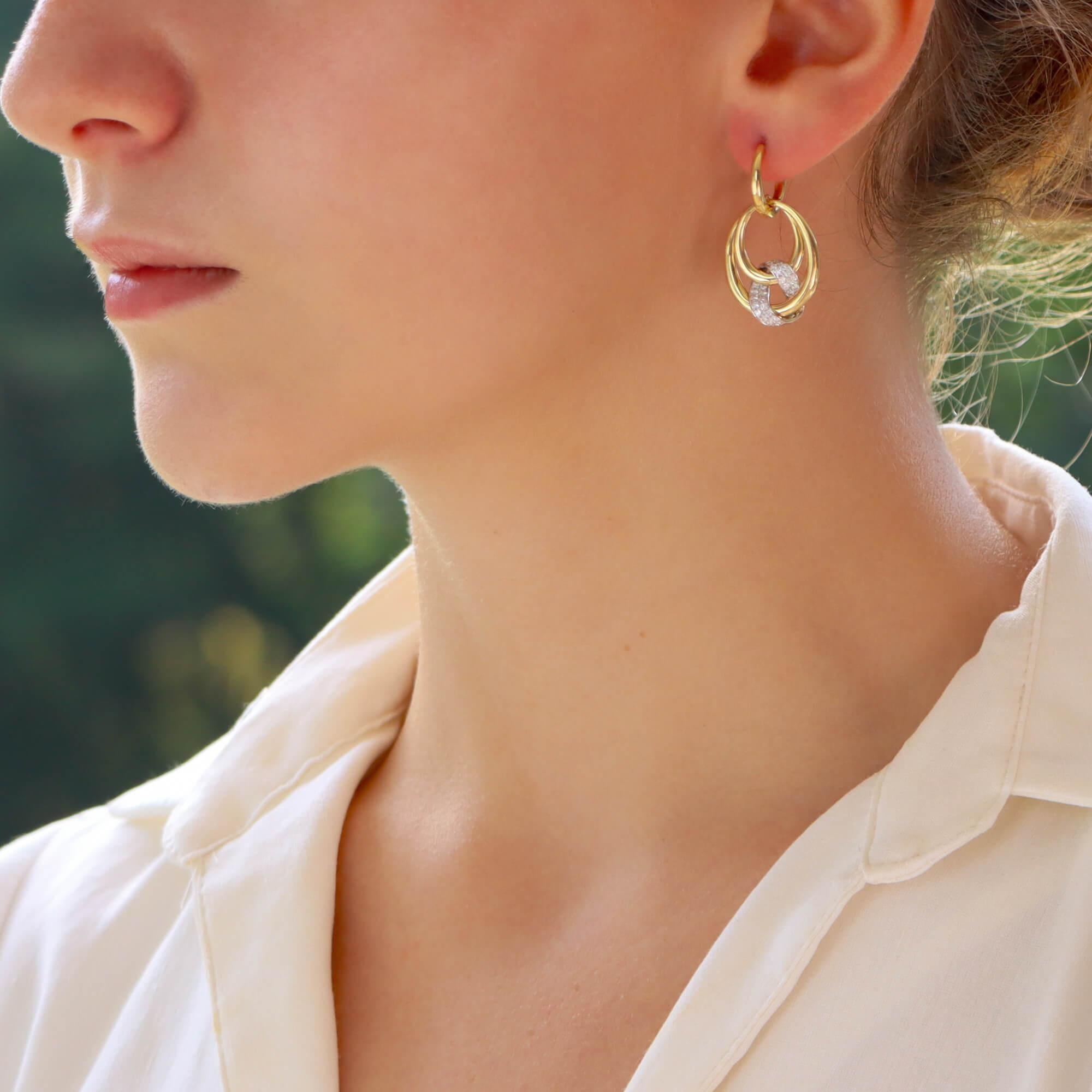 A beautiful contemporary pair of diamond earrings set in 18k yellow gold. 

The earrings are firstly composed of a yellow gold hoop which is secured with a push click fitting. Hanging from this hoop is an intertwined circle design with pave set
