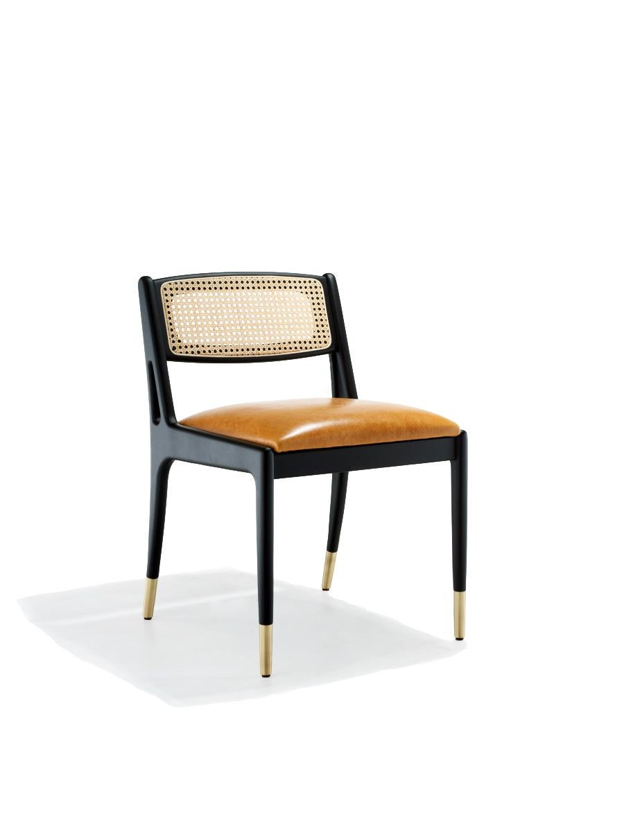 A Mid-Century Modern style dining chairs in ebony finished frame.
Ebony finished wood frame.
Backrest in natural woven cane.
Seat in cognac tan faux leather. 
Polished brass caps.

Dimensions: W 47 cm x D 61 cm x H 77 cm
Materials: Wood, faux