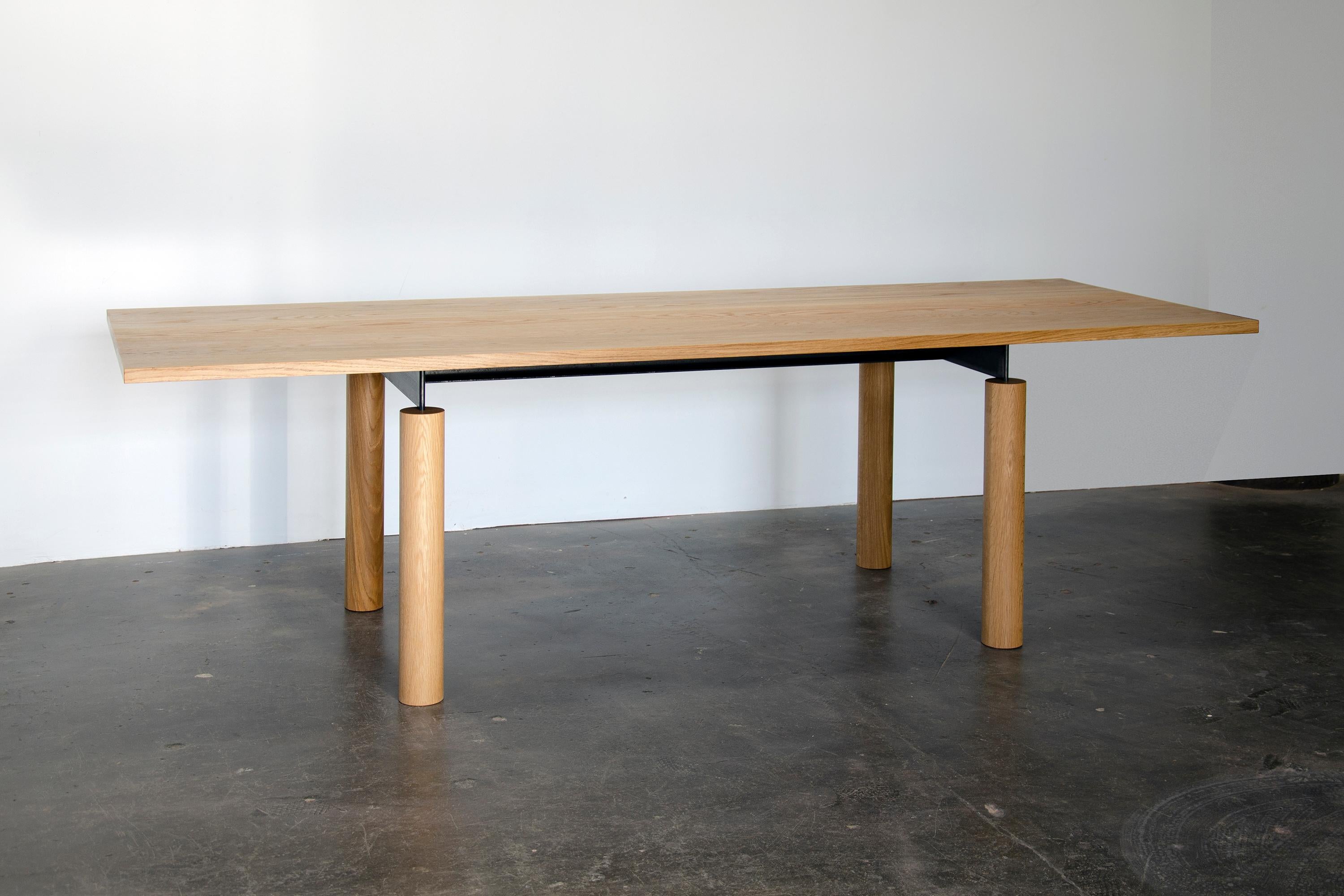 Overpass est une table contemporaine inspirée par les formes simples et la construction robuste des échangeurs d'autoroutes. Soulignant la beauté naturelle du bois massif, un châssis en acier noirci relie gracieusement un plateau épais à des pieds