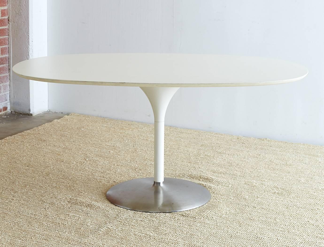 Stunning contemporary oval dining table featuring a tulip shaped base made in the manner and style of Eero Saarinen. Large dining table with an oval shaped top having a cast iron pedestal supported by a brushed steel round bottom. Unique take on an