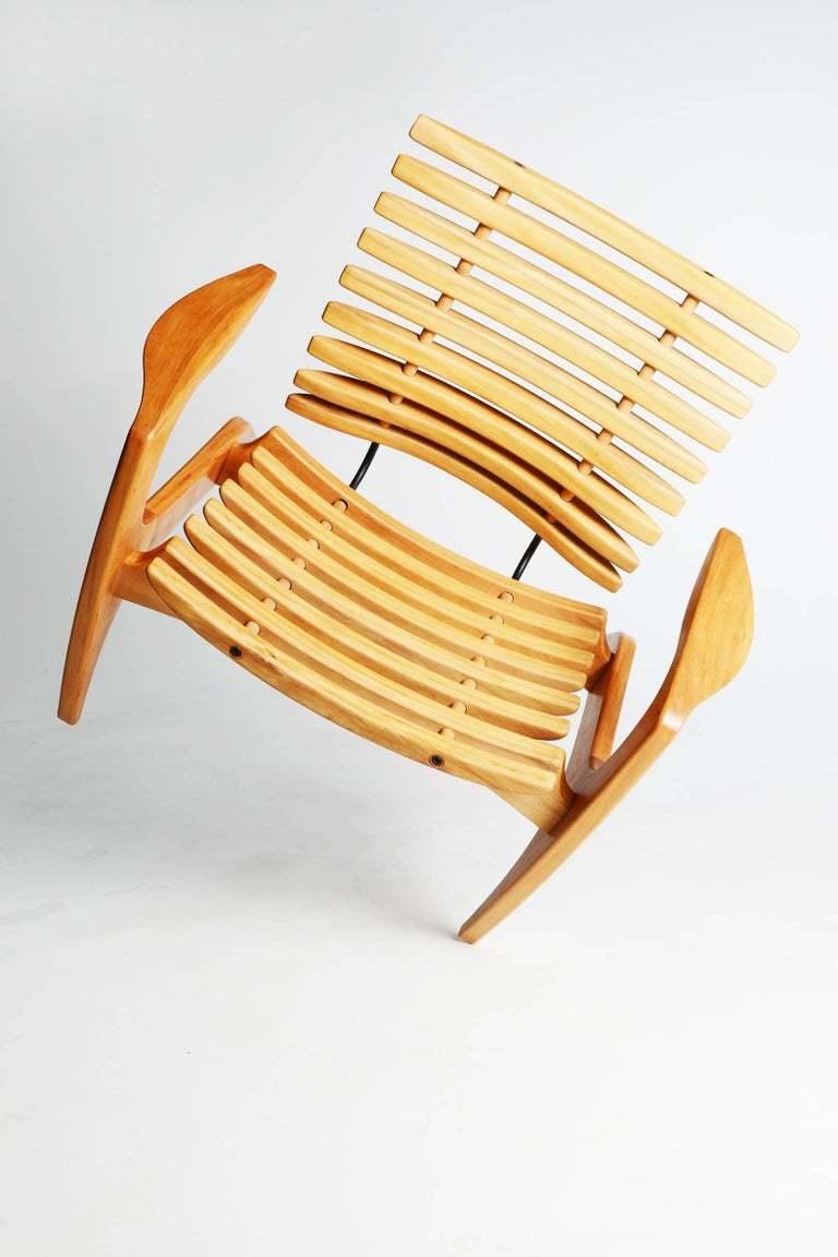 Cette chaise sculpturale conçue par le designer brésilien Henrique Canella se compose d'une structure en bois massif avec une assise et un dossier nervurés, fabriqués avec des techniques d'ébénisterie fines qui ne nécessitent pas l'utilisation de