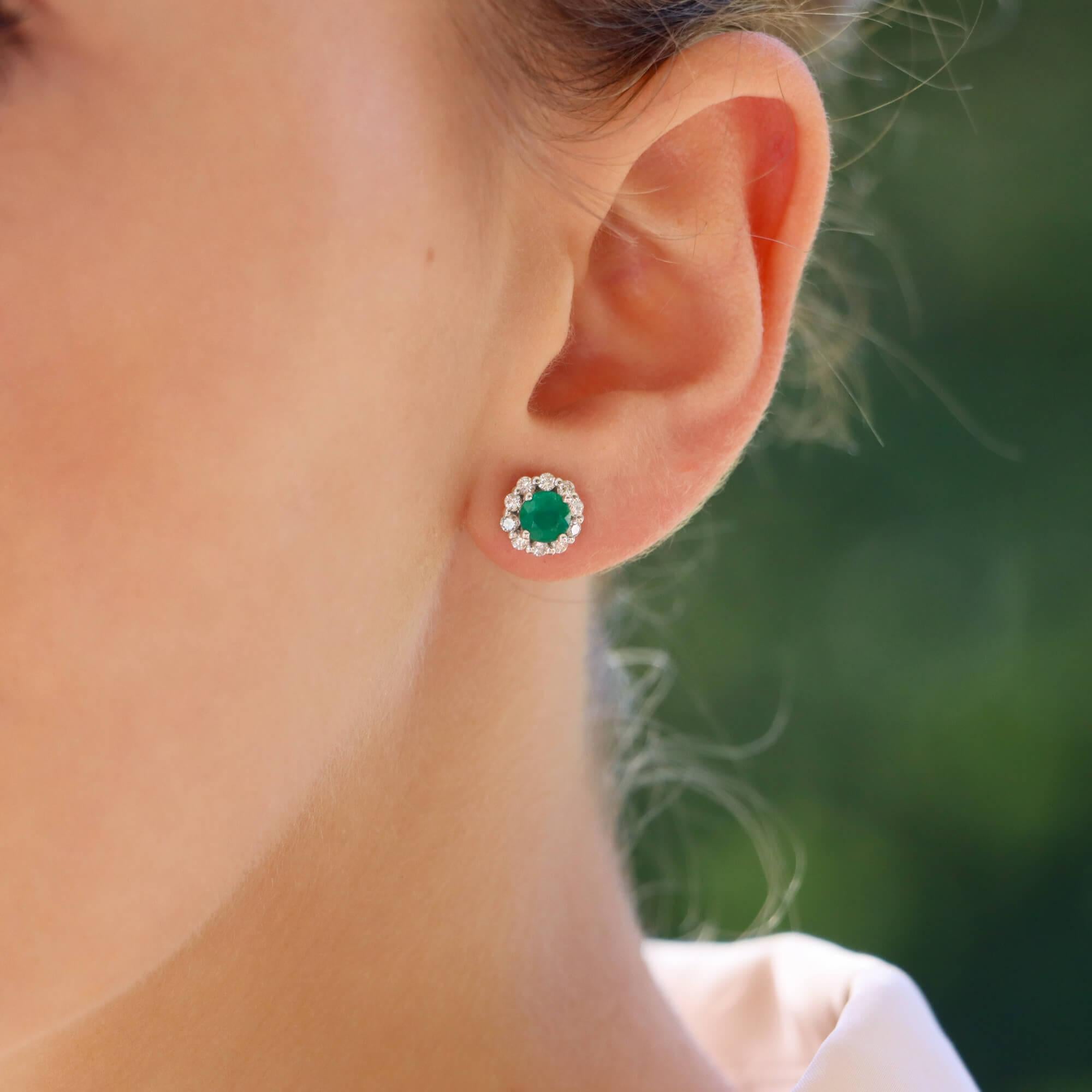 An elegant pair of floral diamond and emerald cluster stud earrings set in 18k white gold.

Each earring depicts a floral motif centrally set with a vibrant green emerald and surrounded by 10 round brilliant cut diamonds. The earrings are secured to