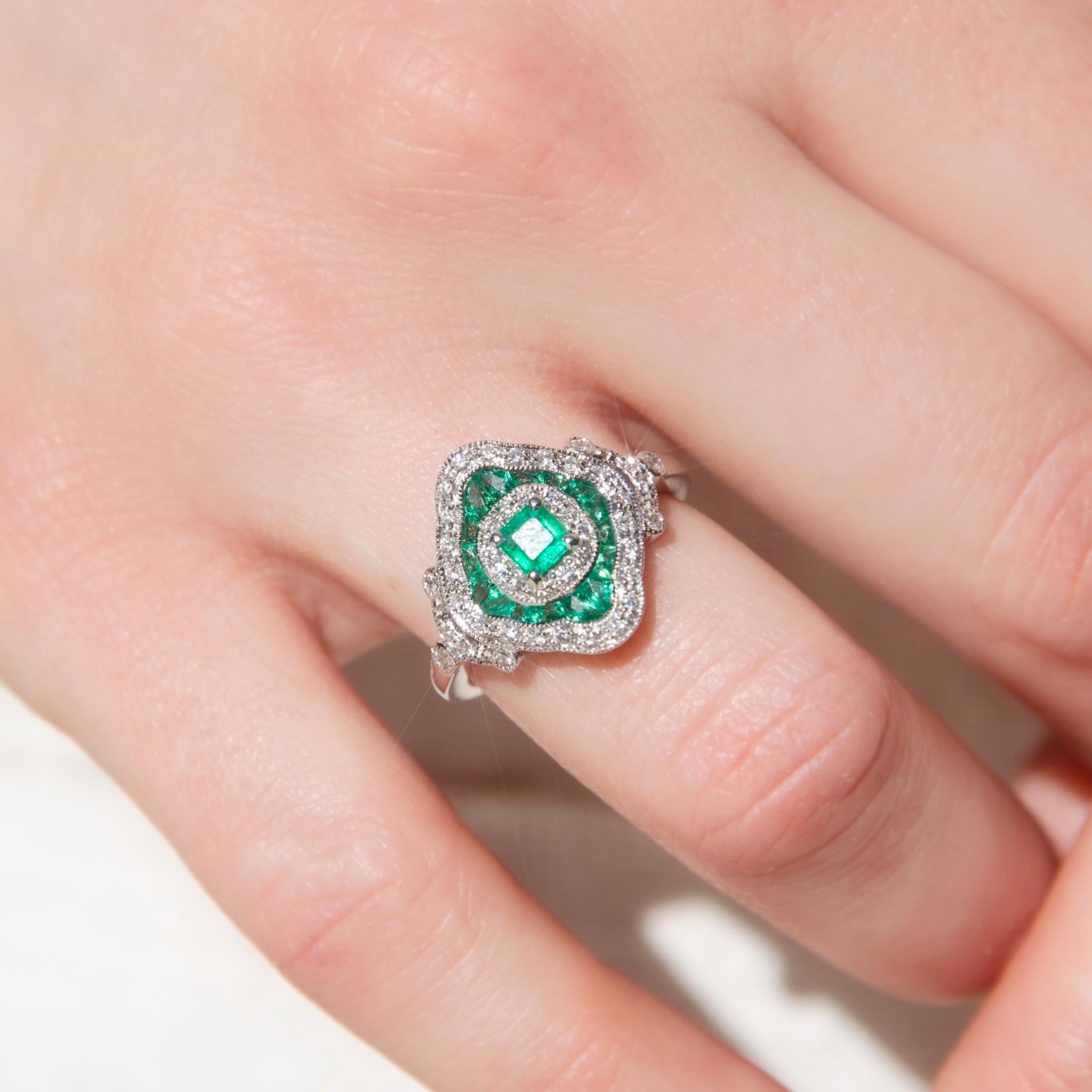 Crafted with perfect love, this wondrous 18 carat white gold ring has a gorgeous milgrain cluster with a central bright green square natural emerald, an inner border of shimmering round diamonds, and two outer diamond-shaped borders, emeralds on the