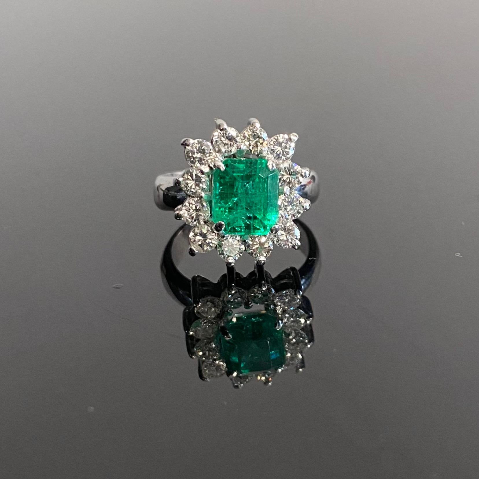 Contemporary Emerald and Diamond Coronet Cluster Engagement Ring in 19.2 Karat White Gold, Portugal, 2010s. Set slightly raised to the centre with an emerald-cut emerald of an intense green color in an open back claw setting, encircled by a single