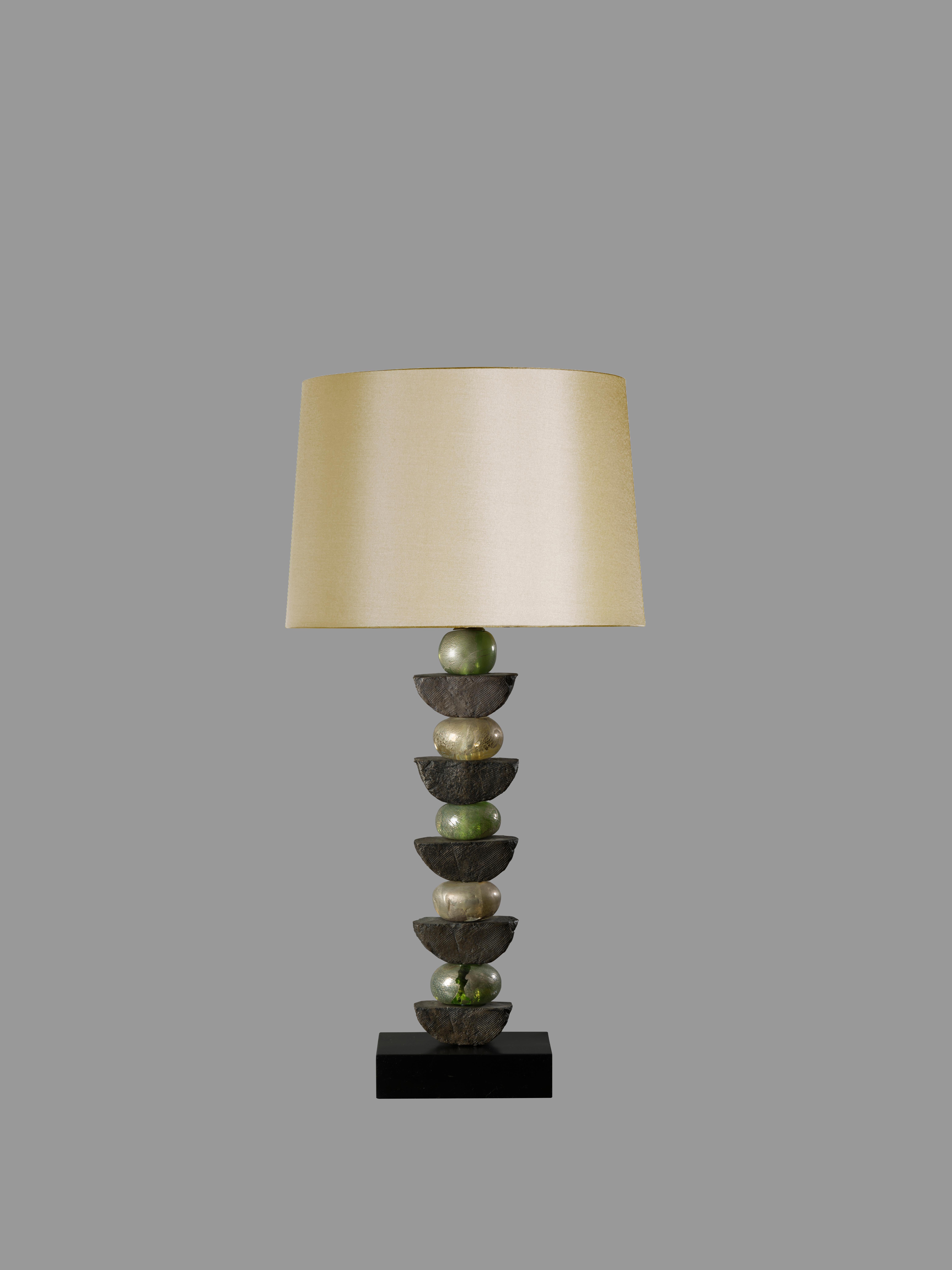 These contemporary Margit Wittig table lamp is mounted on a solid slate bases and feature five mouth blown glass shapes in green with gold and silver leaf and multiple resin hand-cast semi-circles. The bronze resin elements are hand patinated to