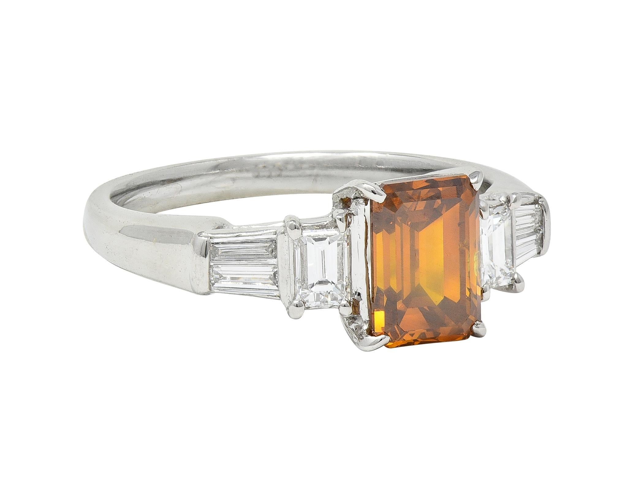 Centering an emerald cut diamond weighing 1.52 carats total 
Transparent medium orangey brown in color
Prong set in basked and flanked by stepped shoulders 
Bar and prong set with baguette and tapered baguette cut diamonds 
Flanked by flared