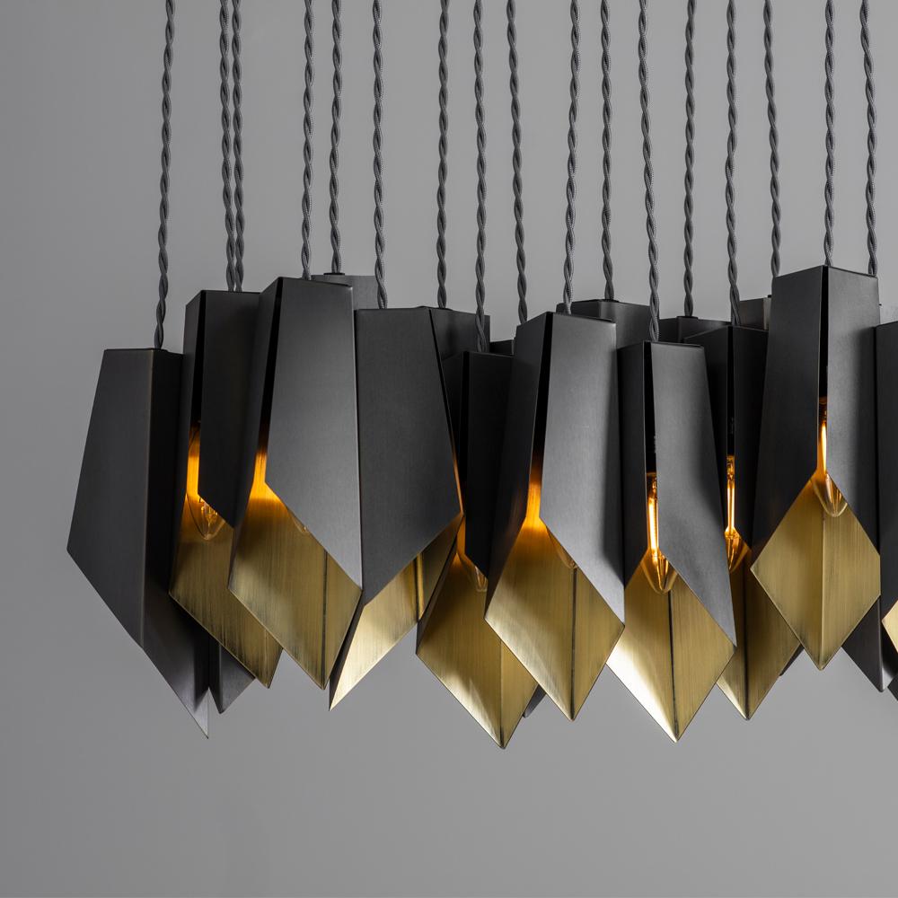 A linear array of folded brass shades, each one patinated to a dark bronze colour and hand-grained on the inside surfaces to reflect the light.

Designed and handmade by Tigermoth Lighting on the banks of the river Thames in the English