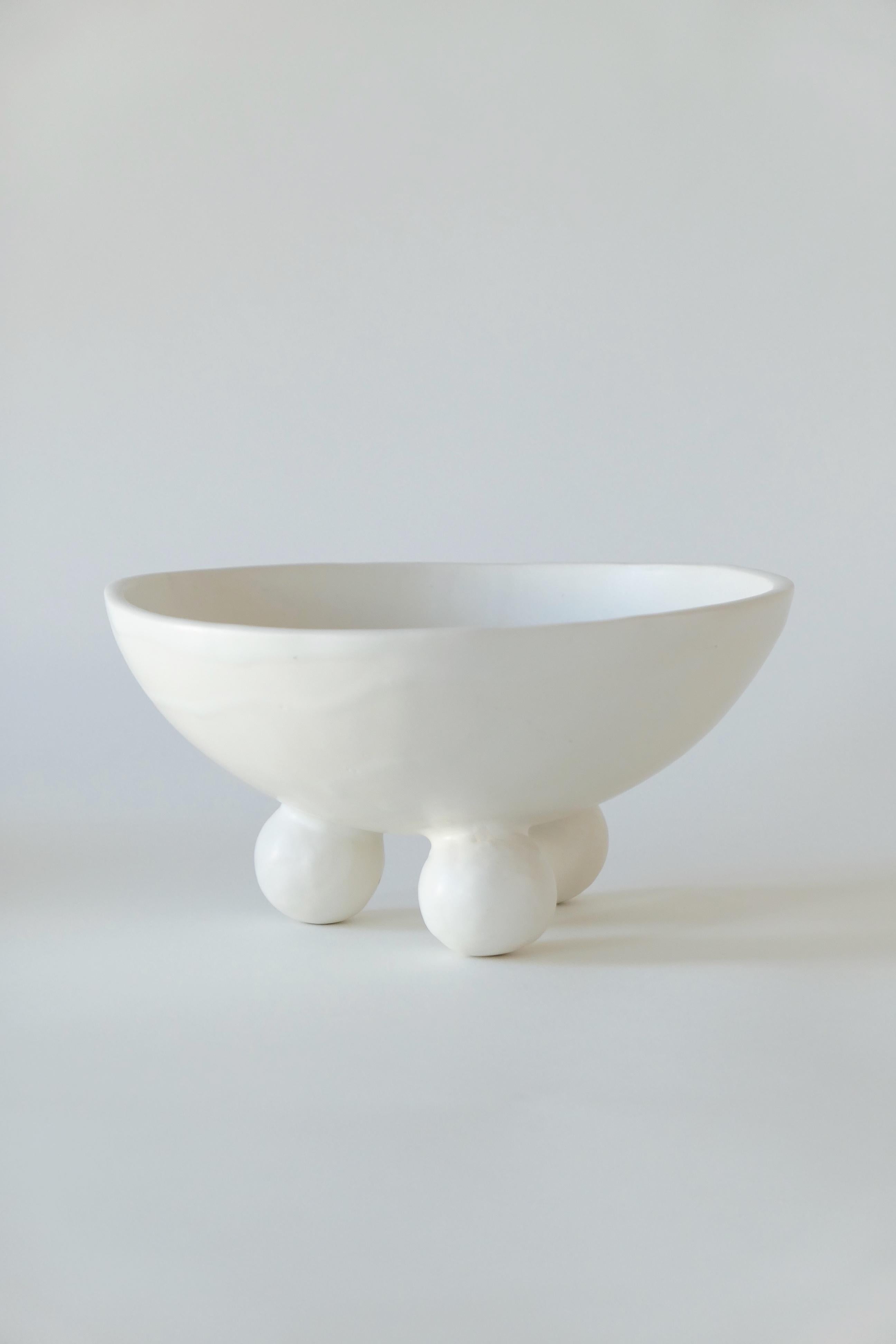 Moderne Schale aus Steingut mit Fuß. Abgeschlossen mit einer weichen, weißen Glasur.

Karina Vieira ist eine in Brooklyn ansässige Keramikerin, die sich auf handgefertigte Gefäße konzentriert. 

Ihr Werk bezieht sich auf verschiedene Stile, berührt