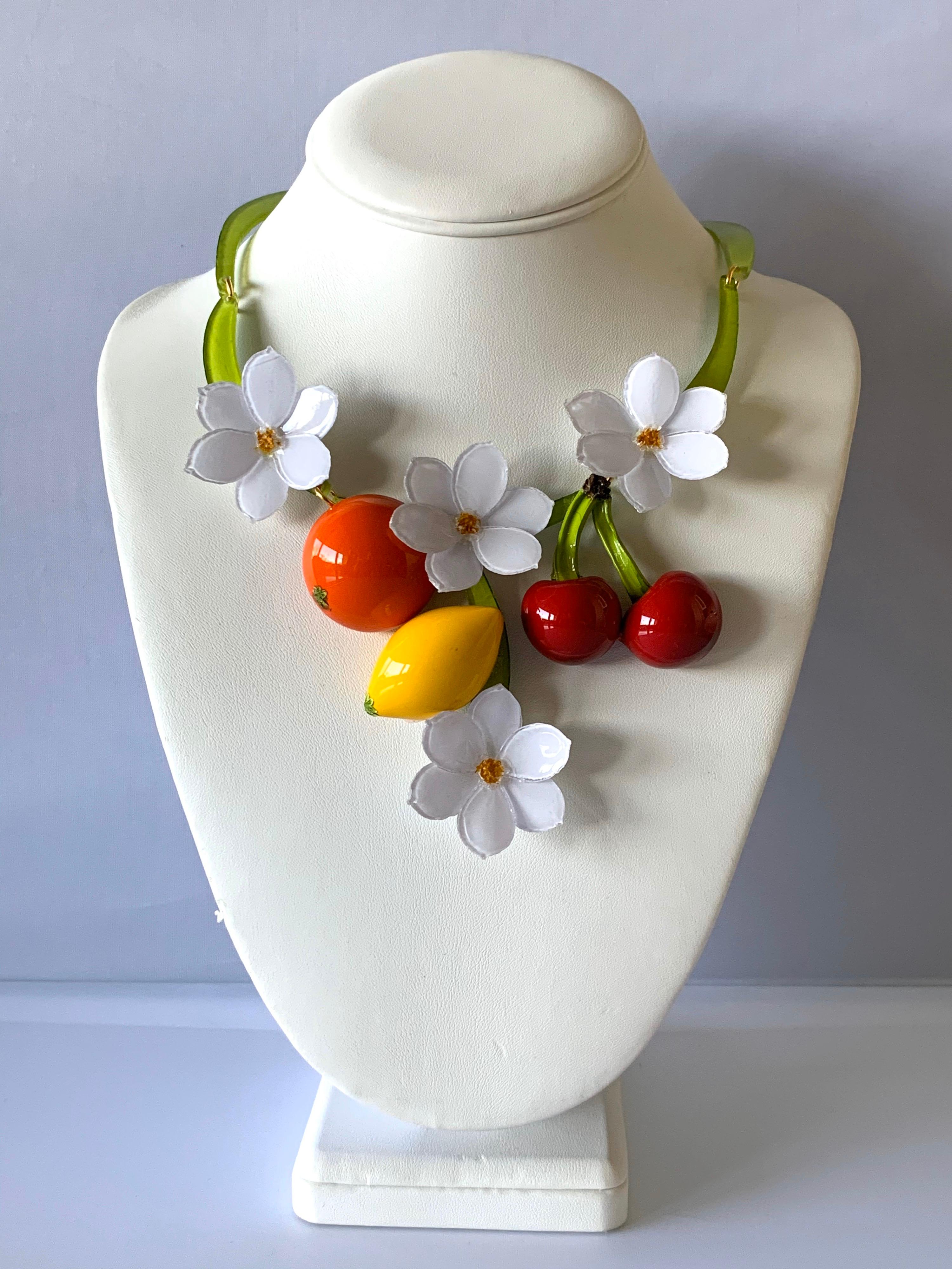 Light and easy to wear, the contemporary handmade adjustable artisanal necklace was crafted in Paris by Cilea. The statement necklace features three-dimensional fruit and white enameline (enamel and resin composite)  flowers. The cherry, orange, and