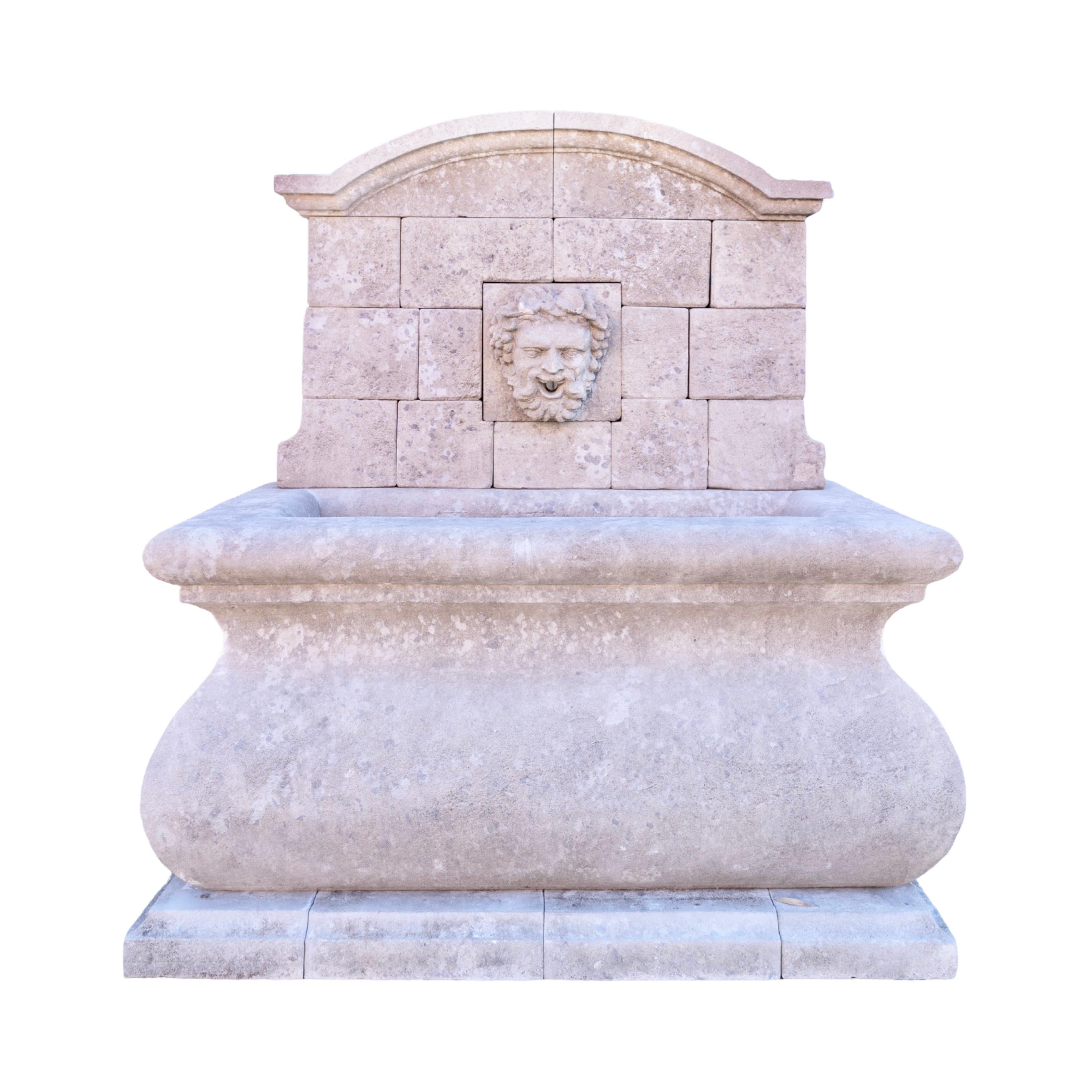 Une fontaine murale contemporaine en pierre calcaire sculptée à la main en France, présentant un mélange raffiné de design classique et moderne. La fontaine est dotée d'un grand bassin rectangulaire aux bords élégamment incurvés, reposant sur une
