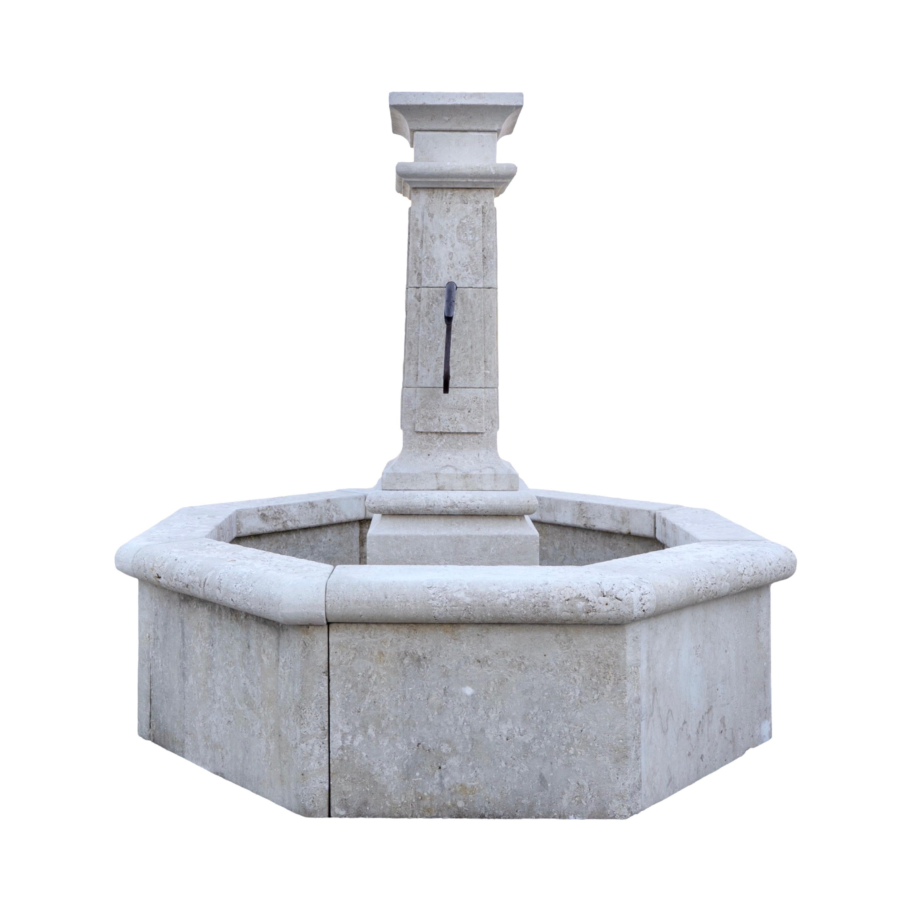 Une fontaine contemporaine en pierre calcaire sculptée à la main en France, dotée d'un bassin géométrique octogonal saisissant. Au centre se dresse une haute colonne rectangulaire avec quatre ouvertures de bec, une de chaque côté, conçues pour des