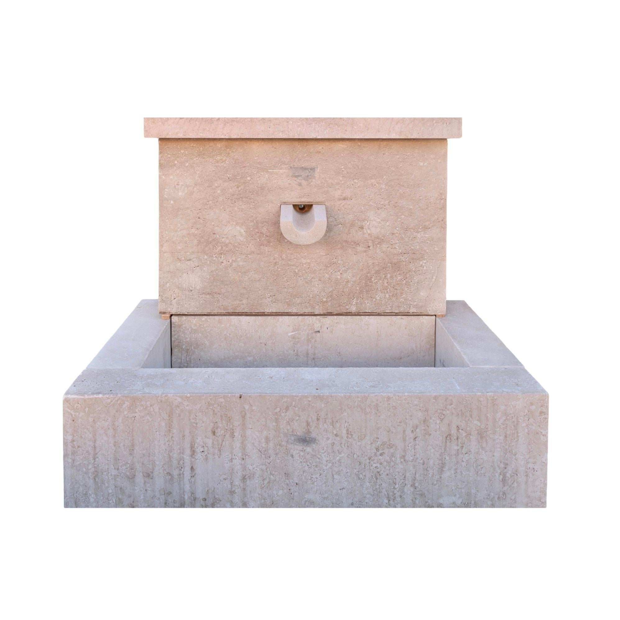 Ein zeitgenössischer, handgeschnitzter Kalkstein-Wandbrunnen aus Frankreich, der ein schlichtes, geometrisches Design mit klaren, definierten Kanten aufweist. Der Brunnen besteht aus einem rechteckigen Becken, das nahtlos mit einer Wandplatte
