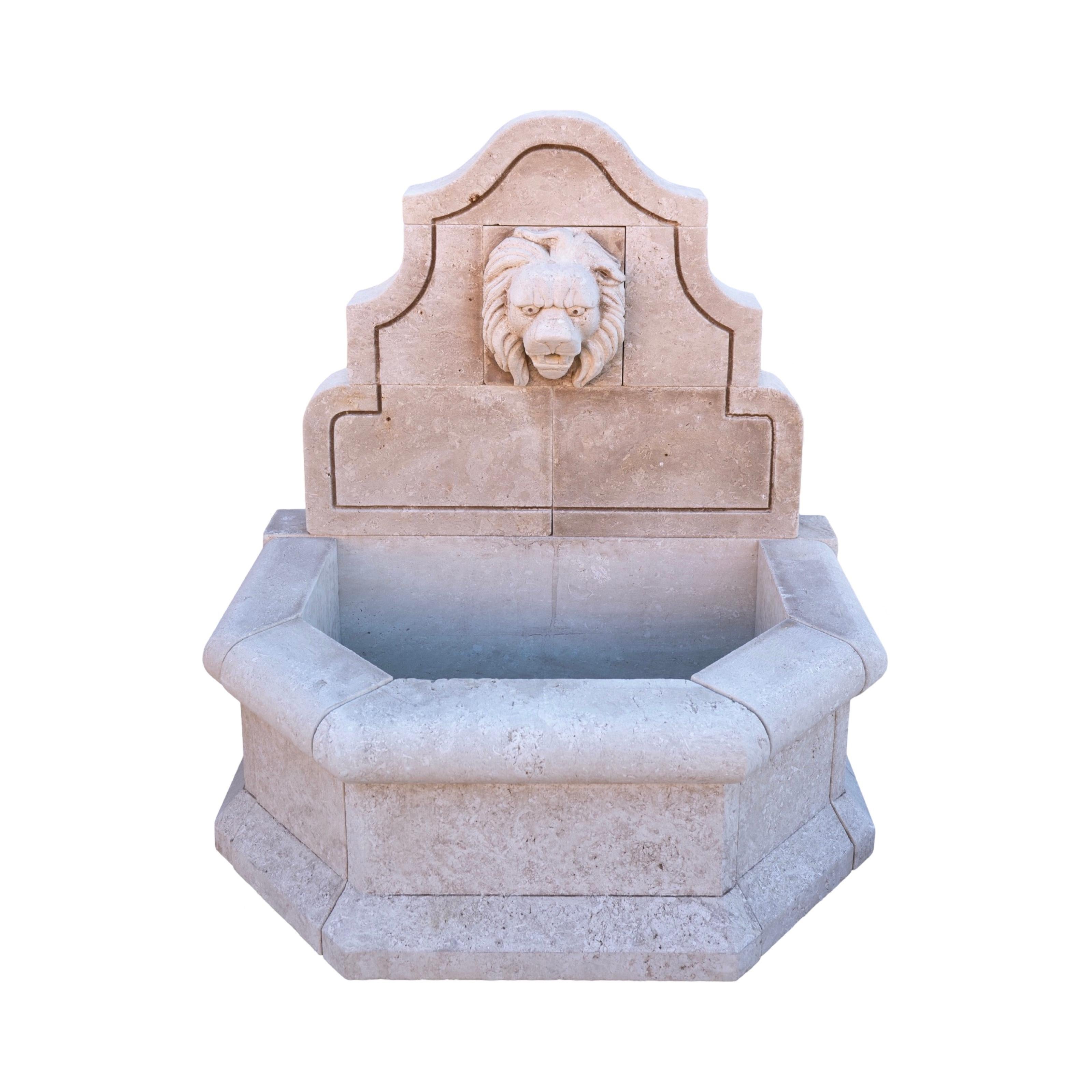 A contemporary hand-carved limestone wall fountain from France, blending geometric precision with classical elegance. The basin features a unique geometric edge design with smooth, sculpted curves, while the wall panel is adorned with gracefully