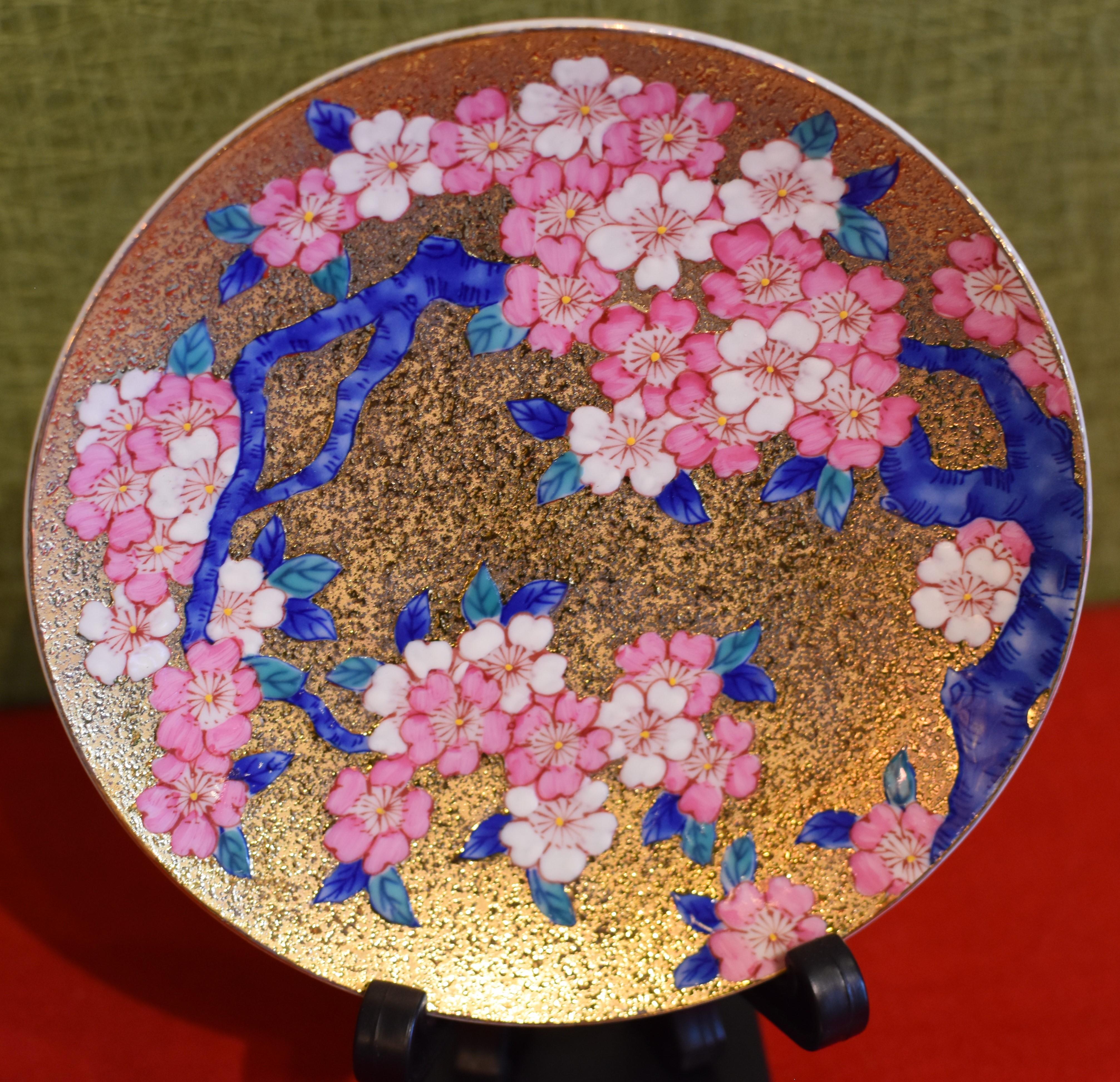 Contemporary gilded signed porcelain cup and saucer, intricately hand-painted in vivid blue, pink and white on an attractive gilded body, featuring auspicious cherry blossoms. This cup and saucer are from a signature series by a highly acclaimed