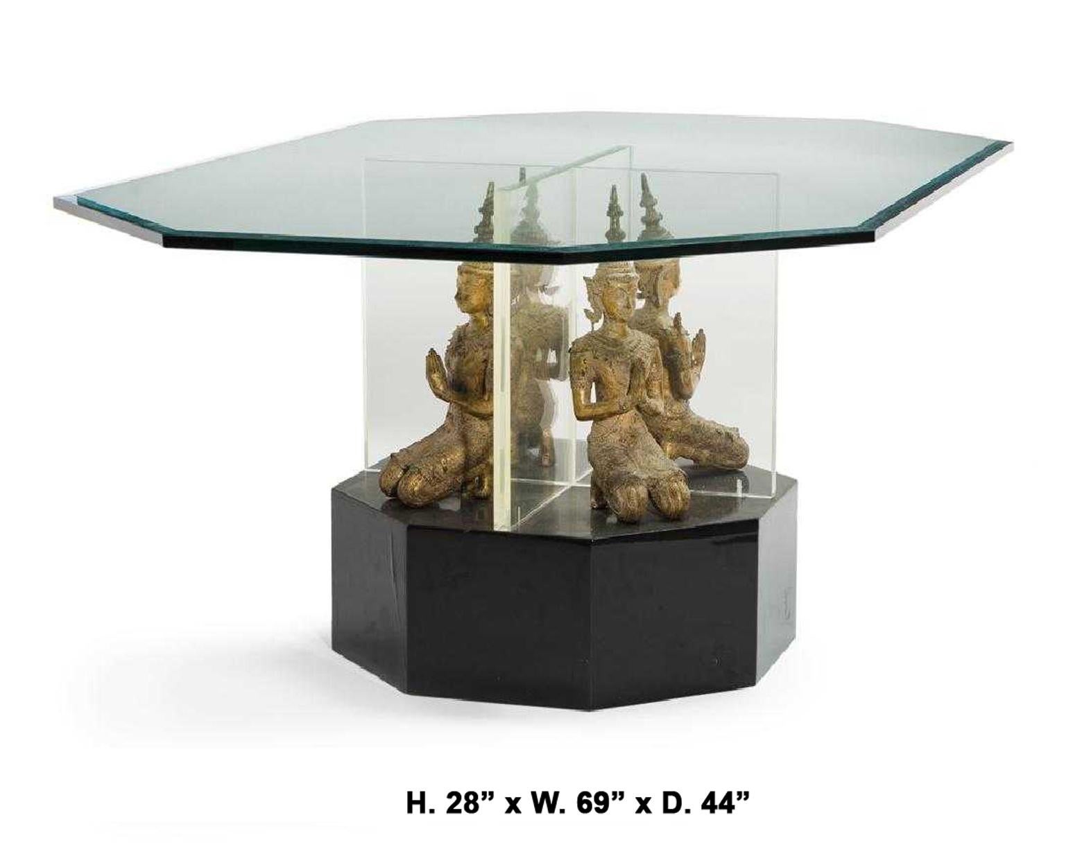 Unique contemporary glass center table with Thai Buddha base. 
The beveled and elongated octagonal glass top rests above a Lucite support with four seated gilt metal Thai Buddas, terminating in a conforming ebonized wooden base. 
20th