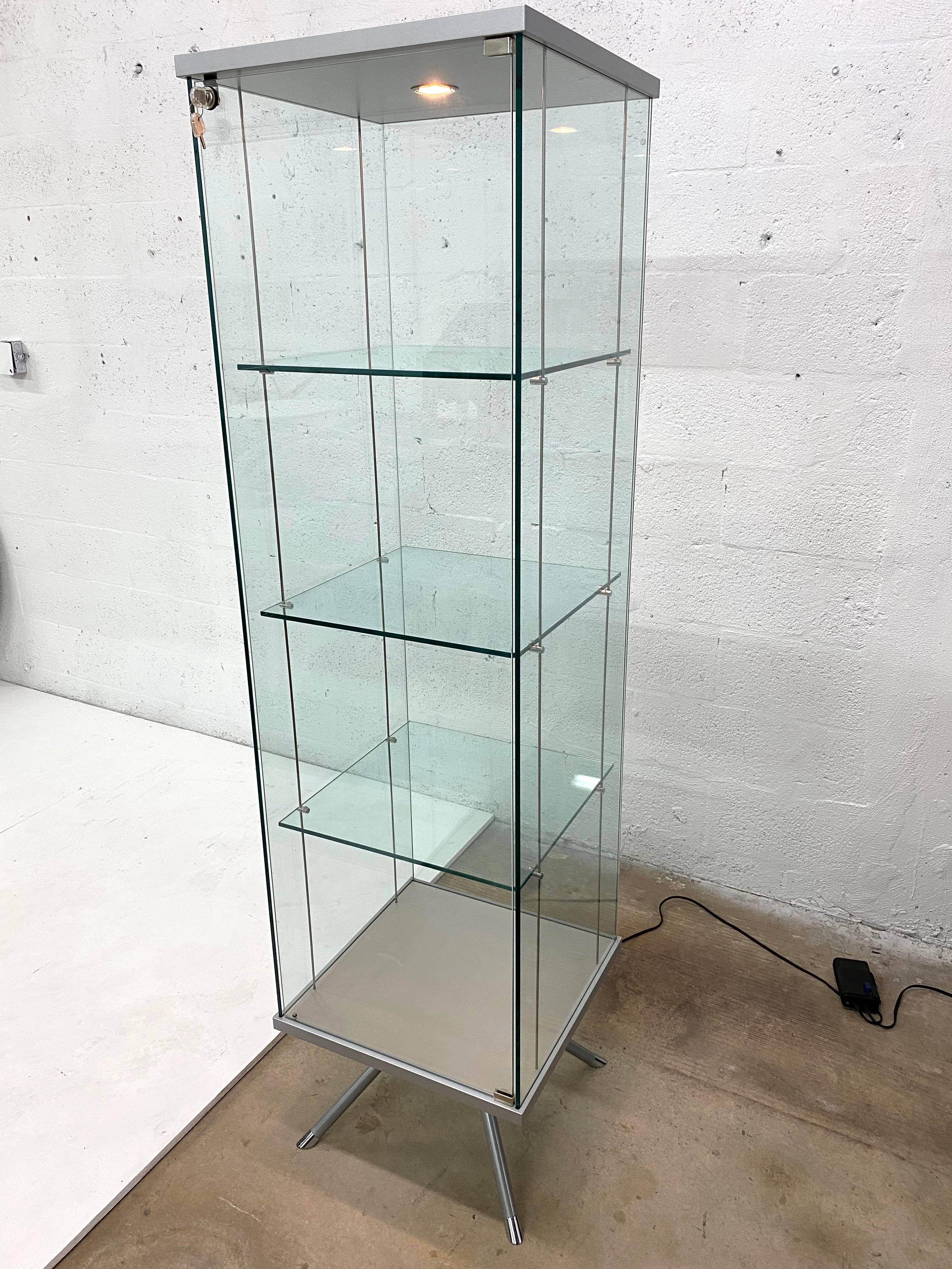 Glass and steel curio display cabinet with suspended glass shelves for art and objects. The lamp is dimmable.