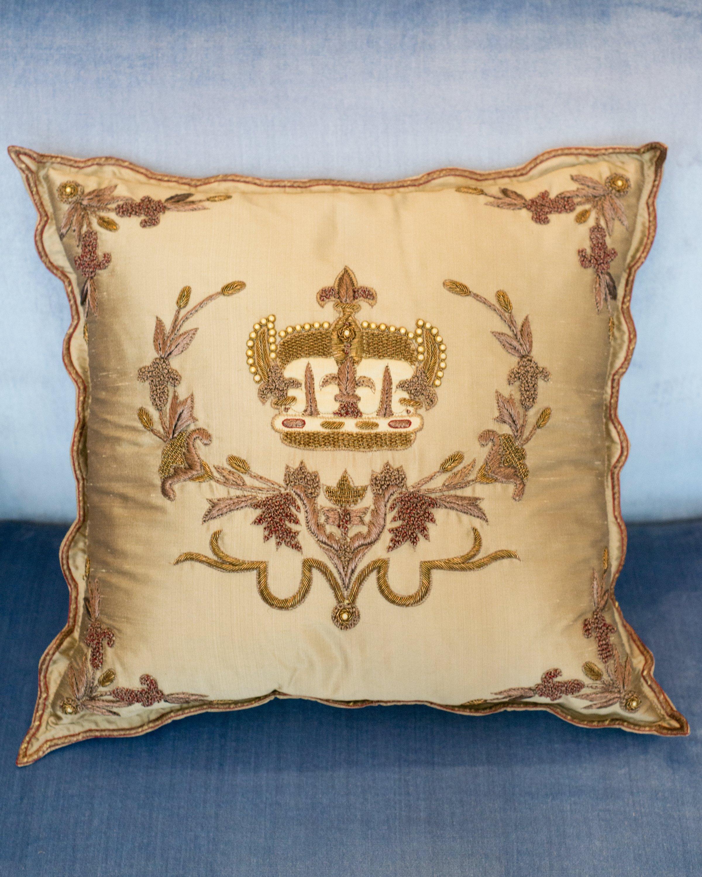 Un oreiller contemporain en soie dorée avec une couronne et un rebord brodés métalliques, fabriqué en Italie.