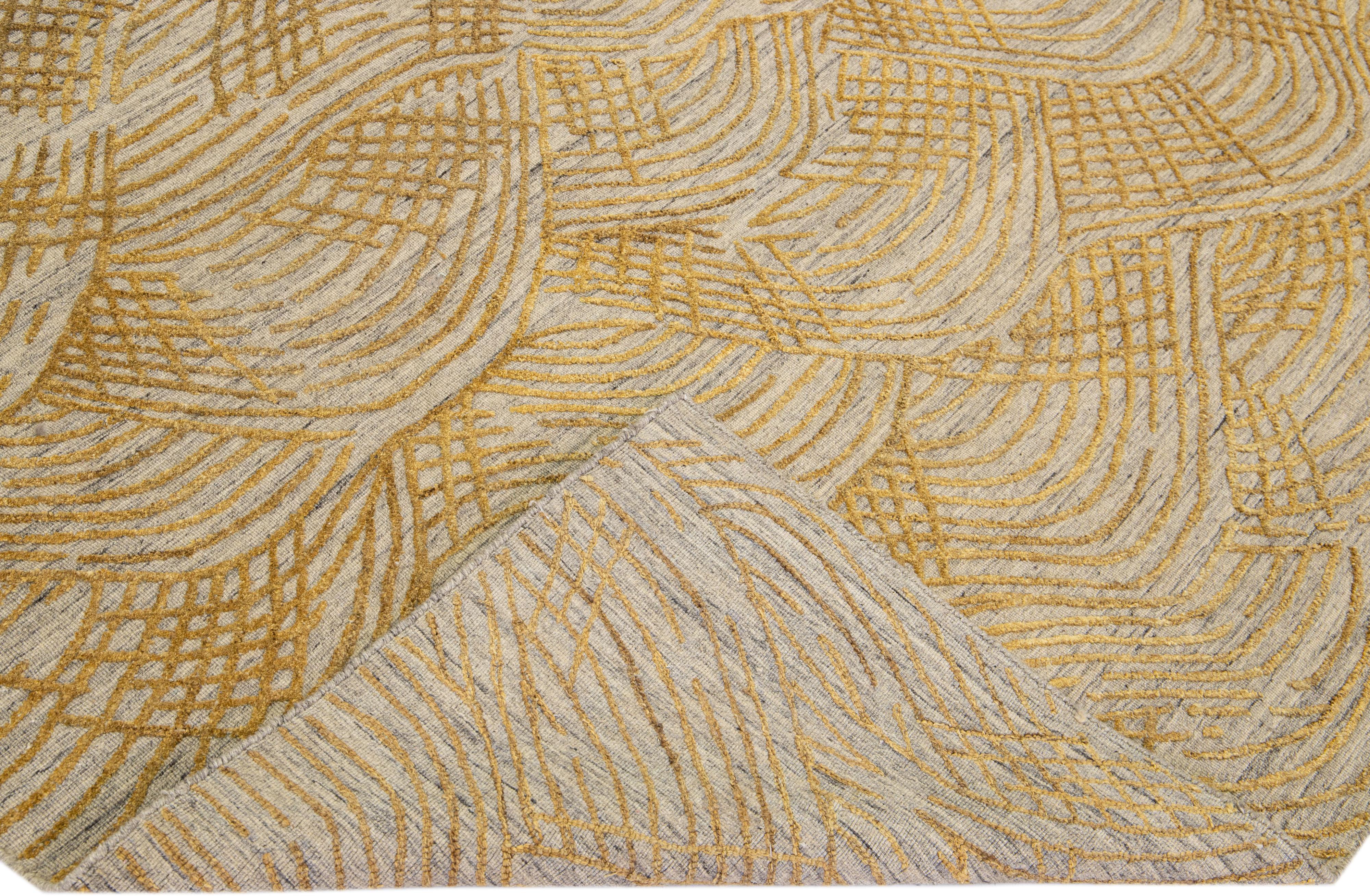 Schöne zeitgenössische Teppiche von Thom Filicia Home Collection. Dieser indische, handgewebte Teppich aus Wolle und Viskose hat ein grau/beiges Feld und goldene Akzente im gesamten Design. 
Thom Filicias Auge für exquisite Details und schöne