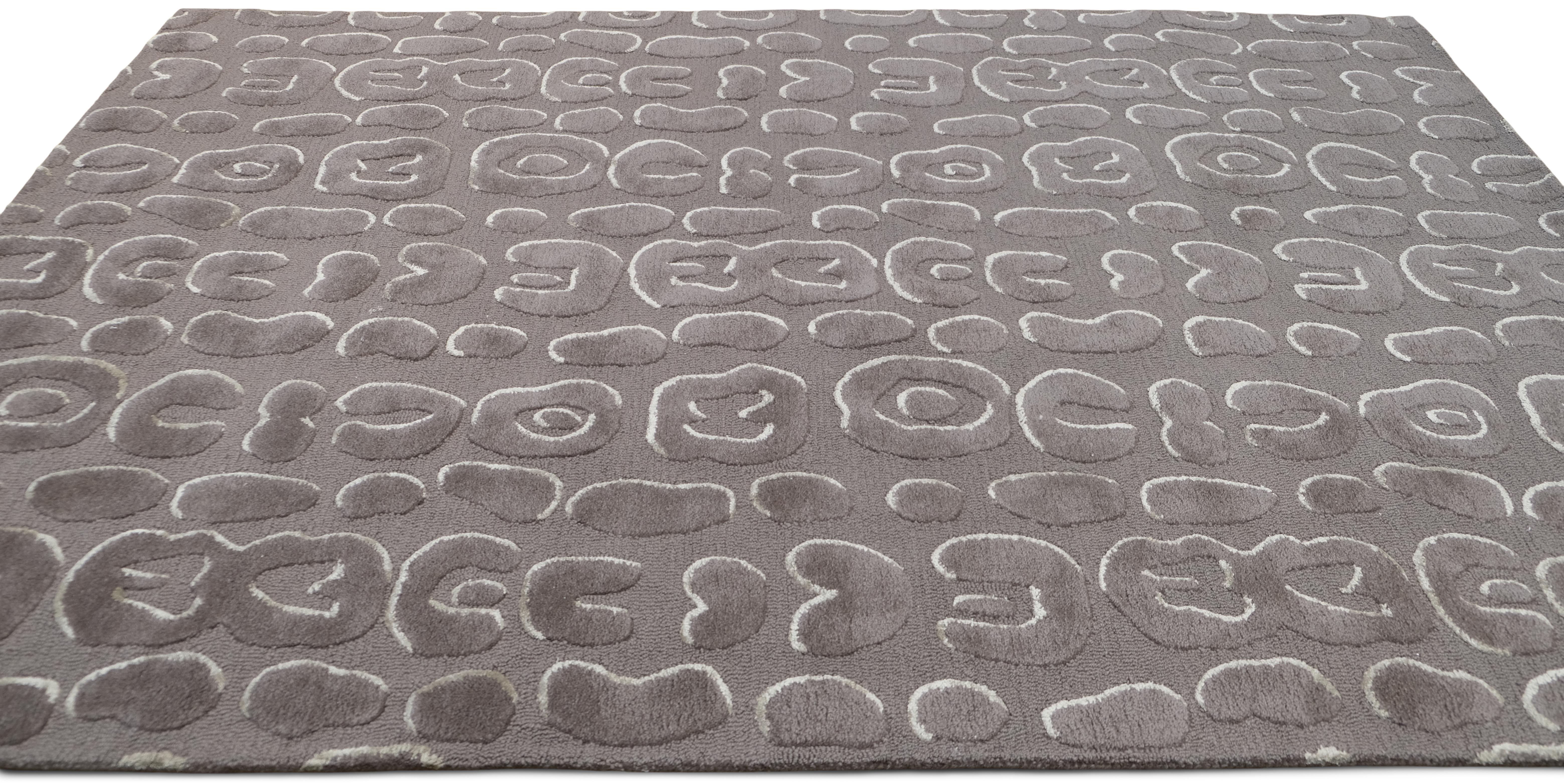 Ce tapis en laine présente un motif abstrait organique inspiré des textures naturelles, présenté dans une palette de couleurs grises sophistiquées. Les poils surélevés ajoutent un effet tactile et dimensionnel, ce qui en fait un élément de style