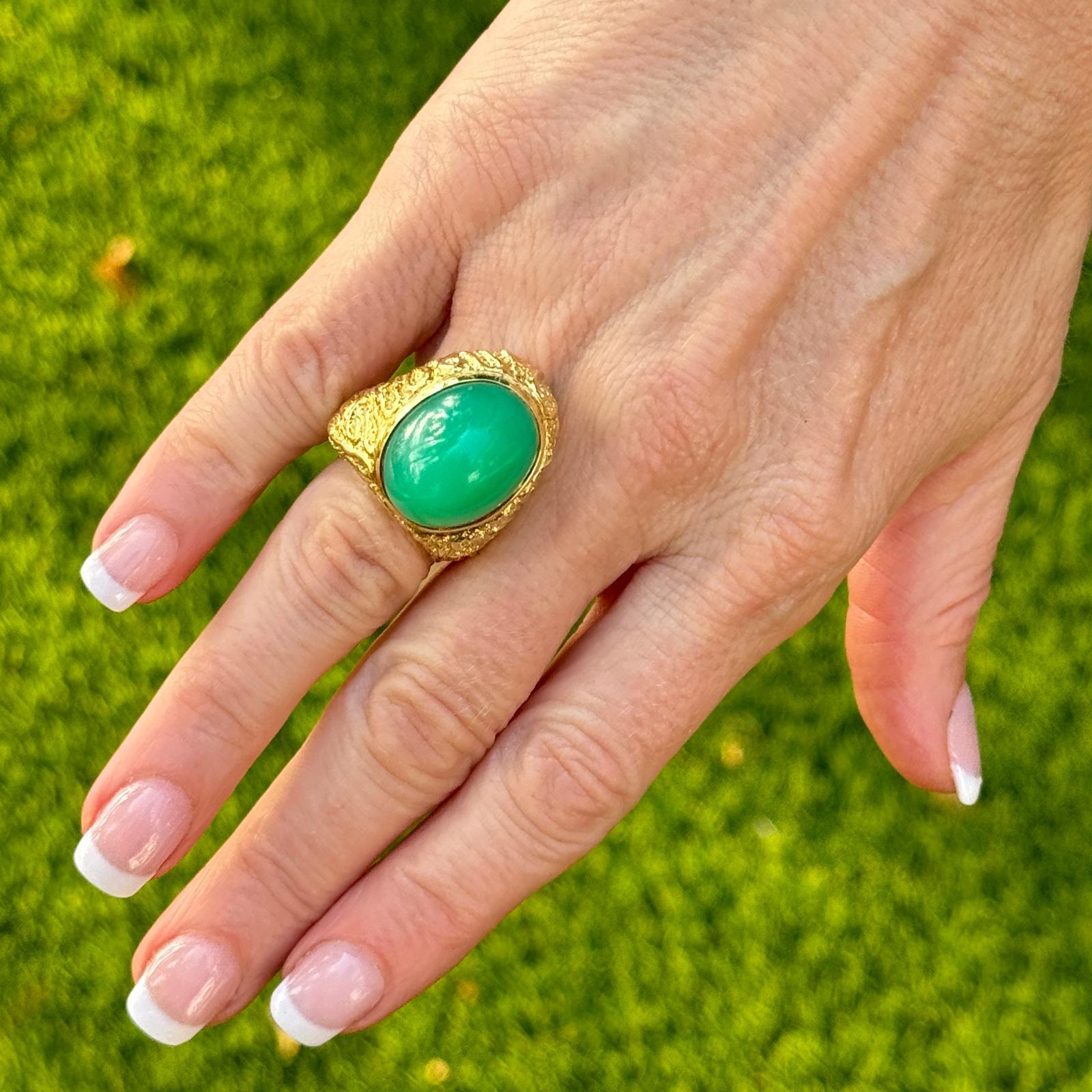 This contemporary ring features a striking design crafted from textured 18 karat yellow gold, giving it a luxurious and distinct appearance. The focal point of the ring is a mesmerizing chrysophase cabochon, characterized by its smooth, rounded