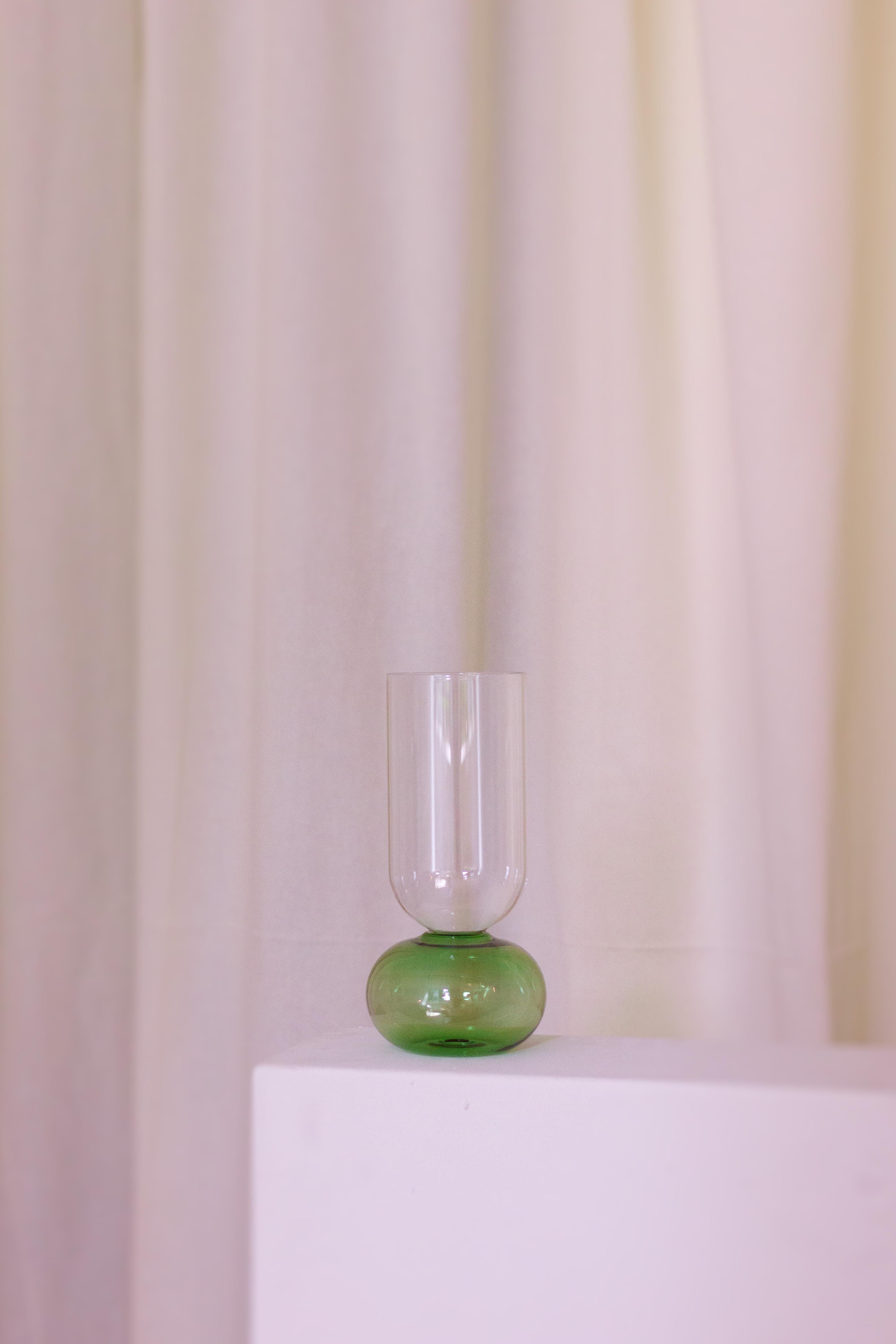 Diese bezaubernde, handgefertigte Vase aus feinem Kristall ist ein Schaufenster der reinen Volumen. Ihre elegante Silhouette besteht aus einem kugelförmigen, blauen Sockel, der den zylindrischen, klaren Körper trägt. Nach traditionellen Techniken